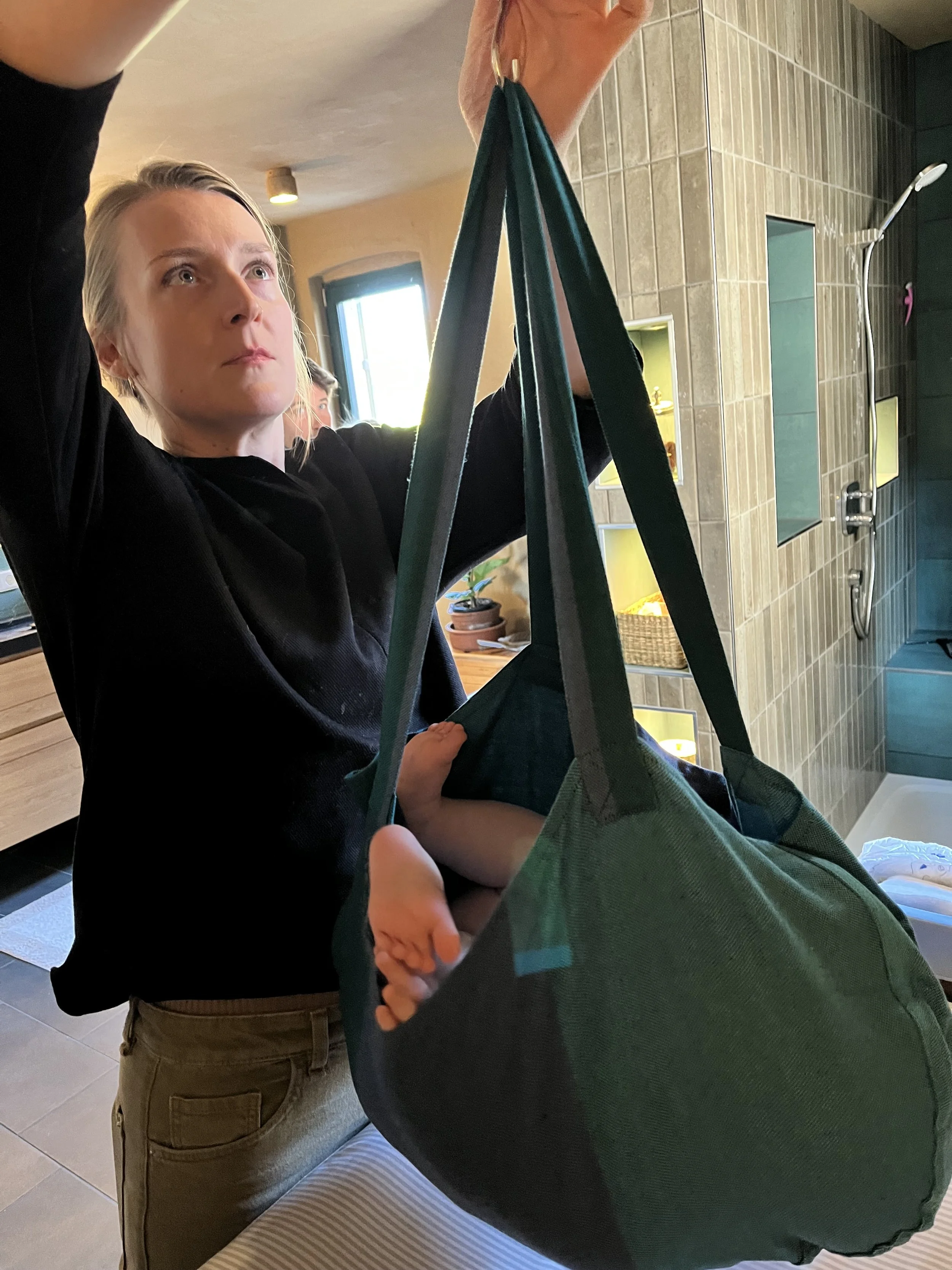 Eine Frau wiegt ein Baby in einer Tragetasche im Badezimmer.