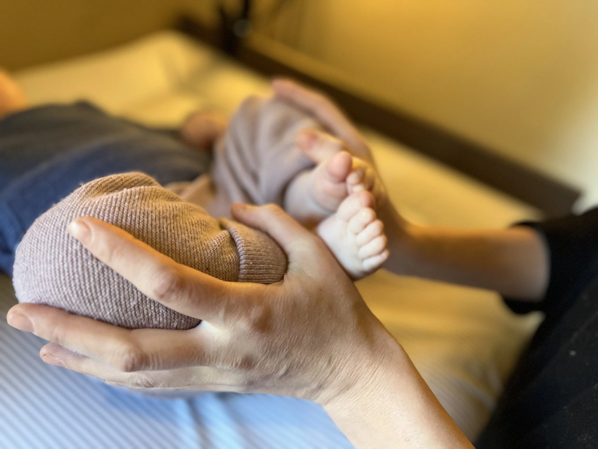 Nahaufnahme einer erwachsenen Hand, die ein kleines Baby anfasst, während es auf einem Wickeltisch liegt.