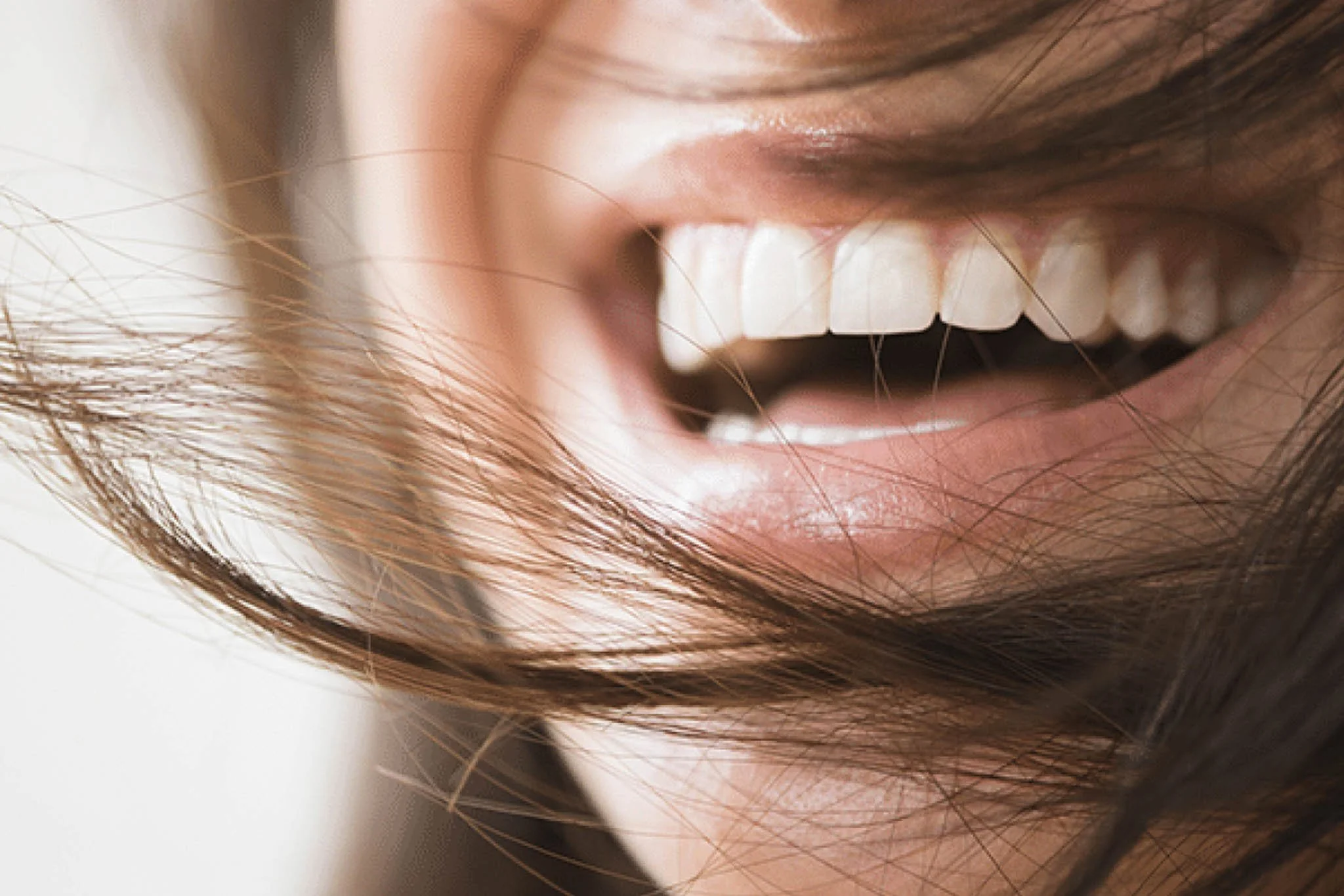 Gros plan d'une personne souriante avec les dents visibles, entourée de cheveux bruns.