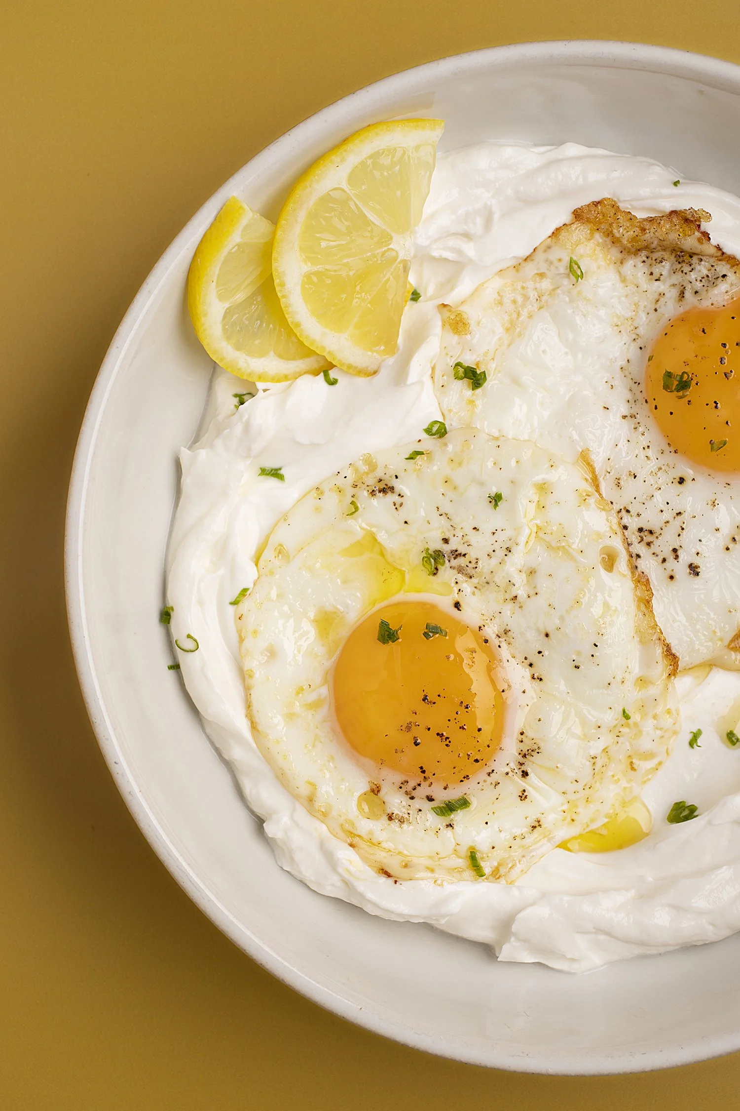 Bowl of two sunny-side-up eggs topped with pepper and chopped green herbs