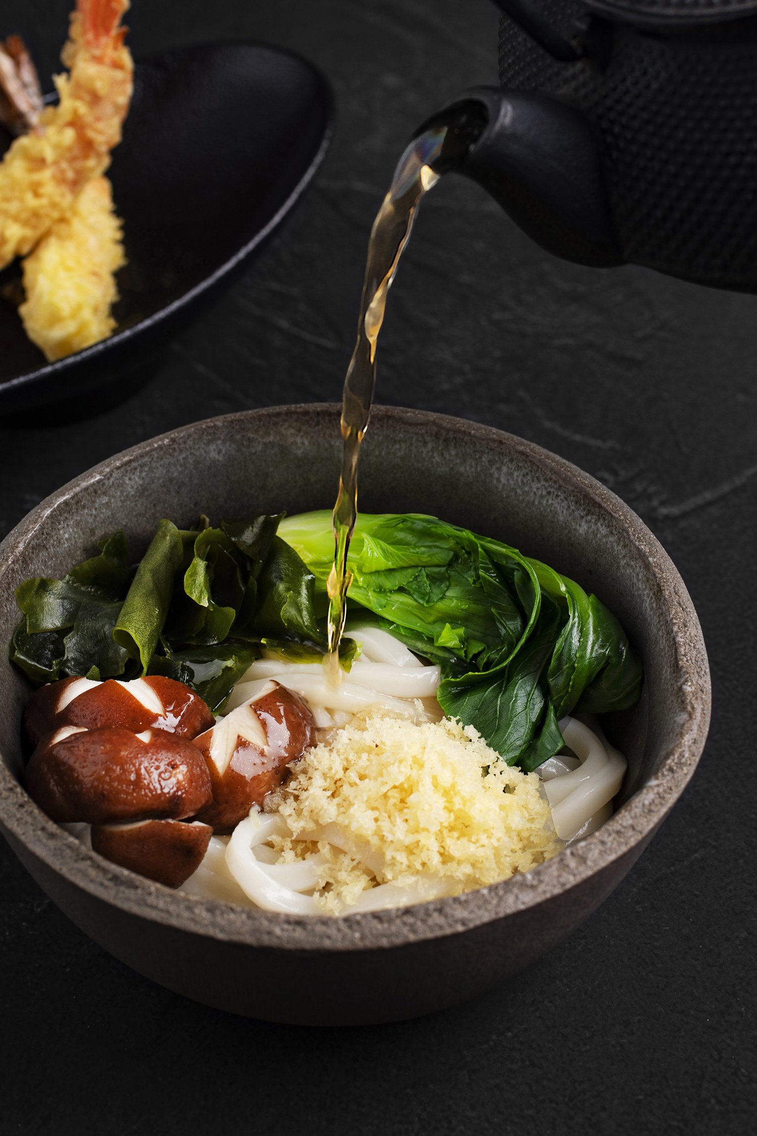 Bowl of udon noodles with spinach, shiitake mushrooms, grated cheese, and broth