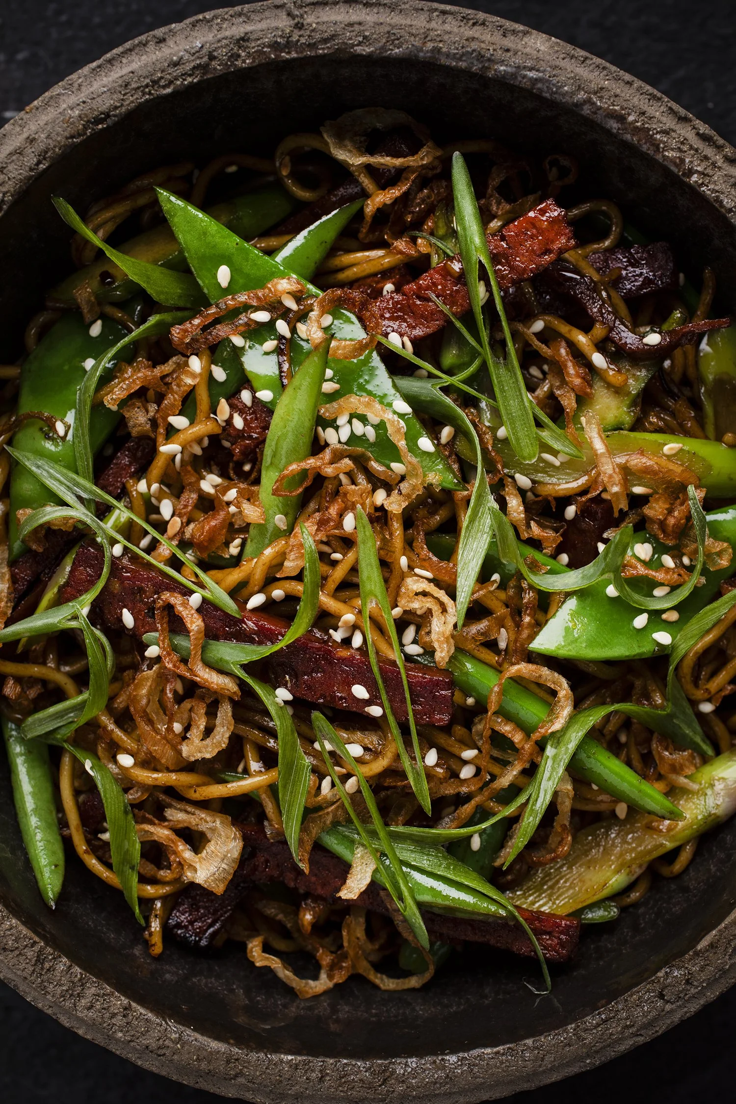 Close-up of a bowl of Asian-style noodles with green vegetables, sliced meat, and sesame seeds