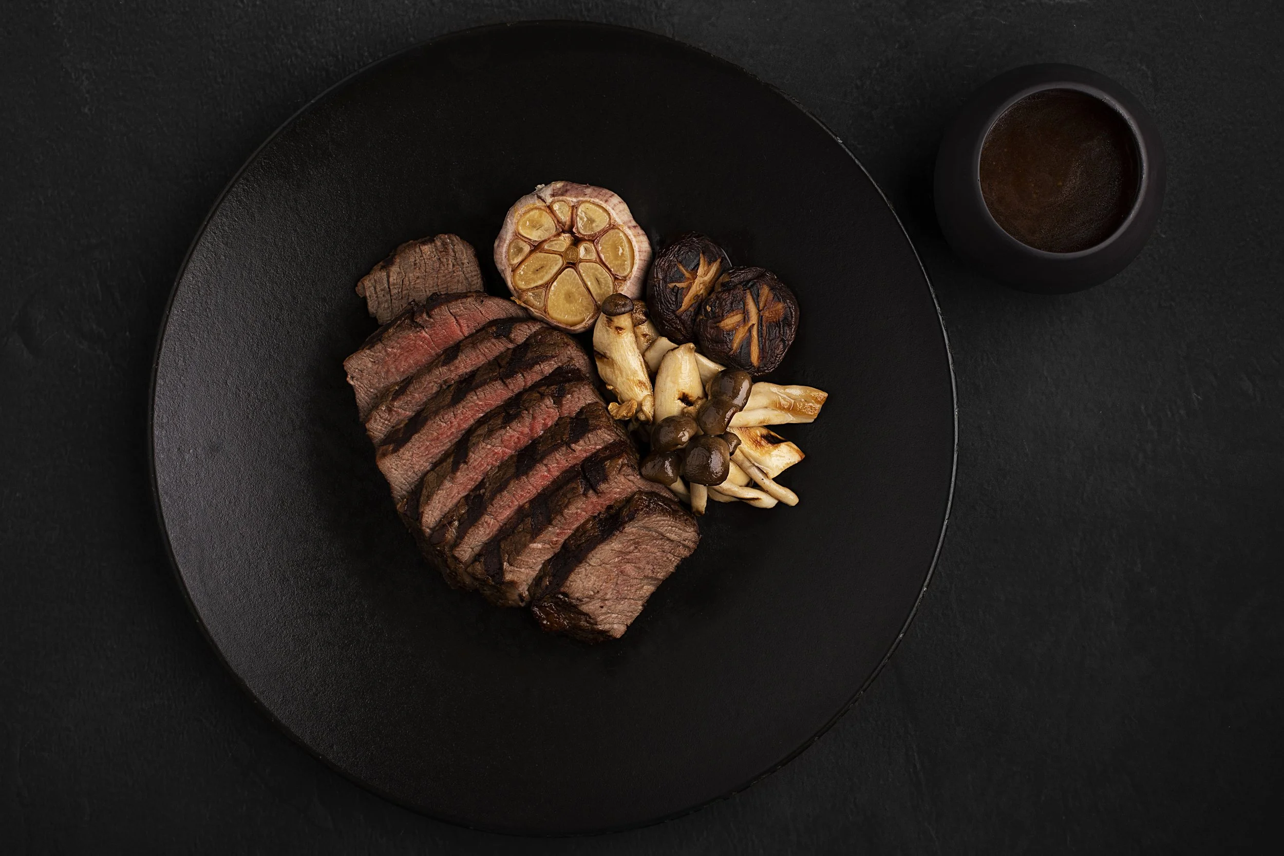 Sliced medium-rare steak with grilled mushrooms, garlic, lemon