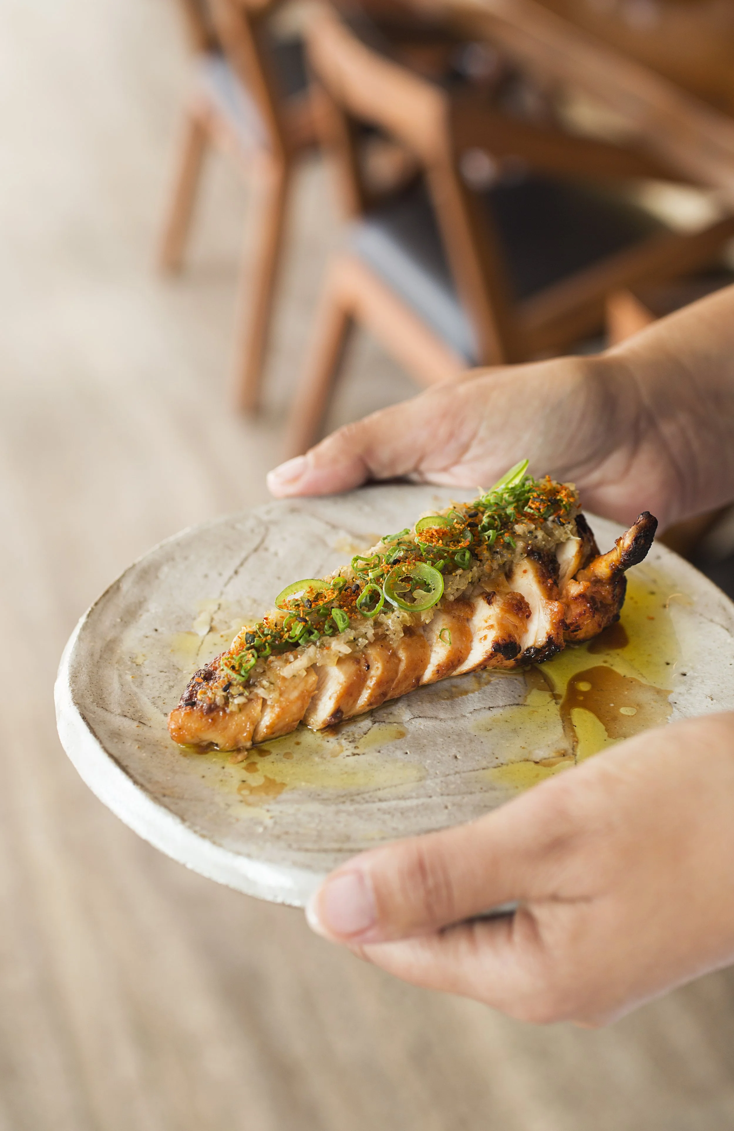 Person holding a stone plate with grilled chicken topped with green onions, sauce, and seasoning
