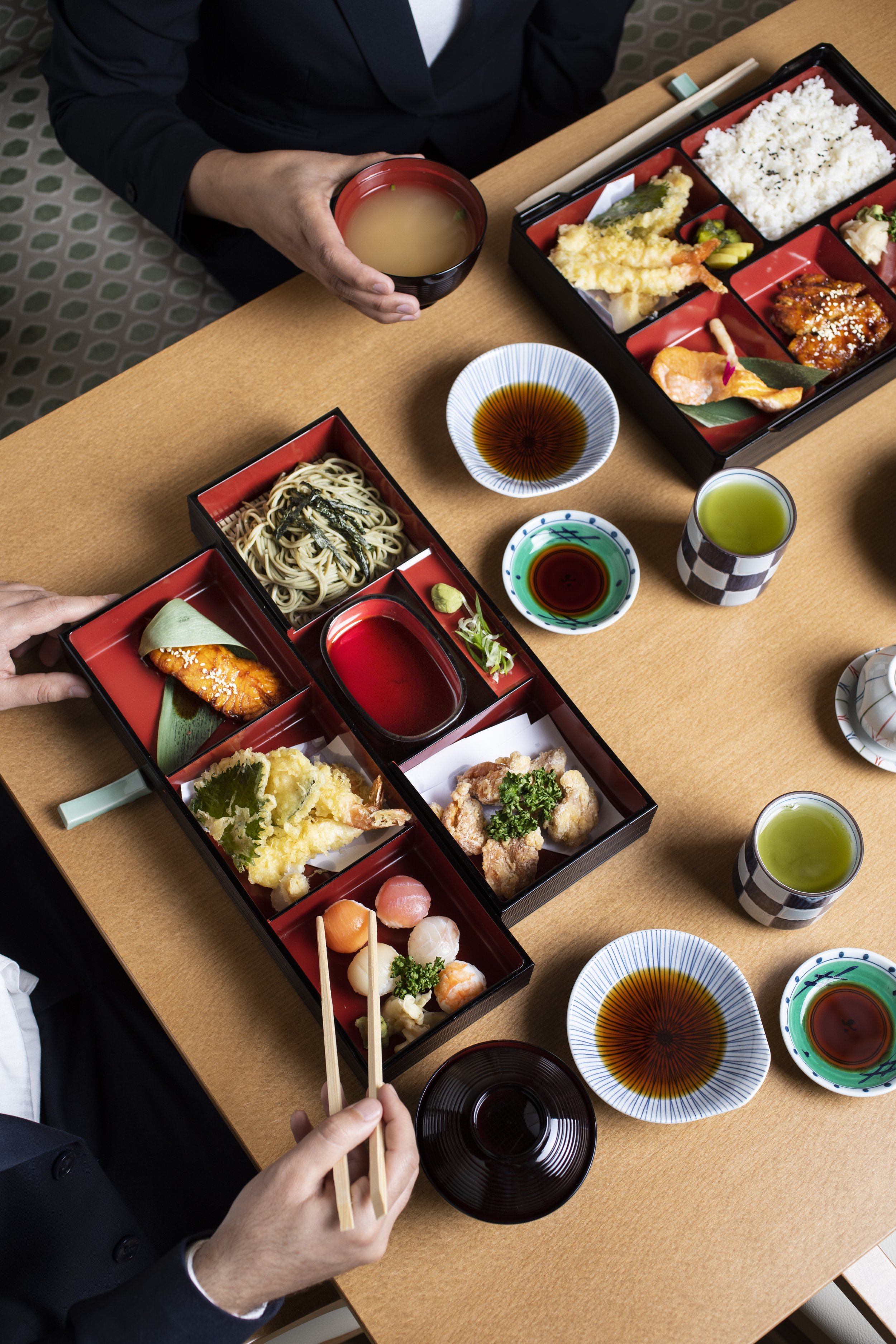 A traditional Japanese meal with bento boxes containing tempura, sushi, sashimi, rice, and soba noodles
