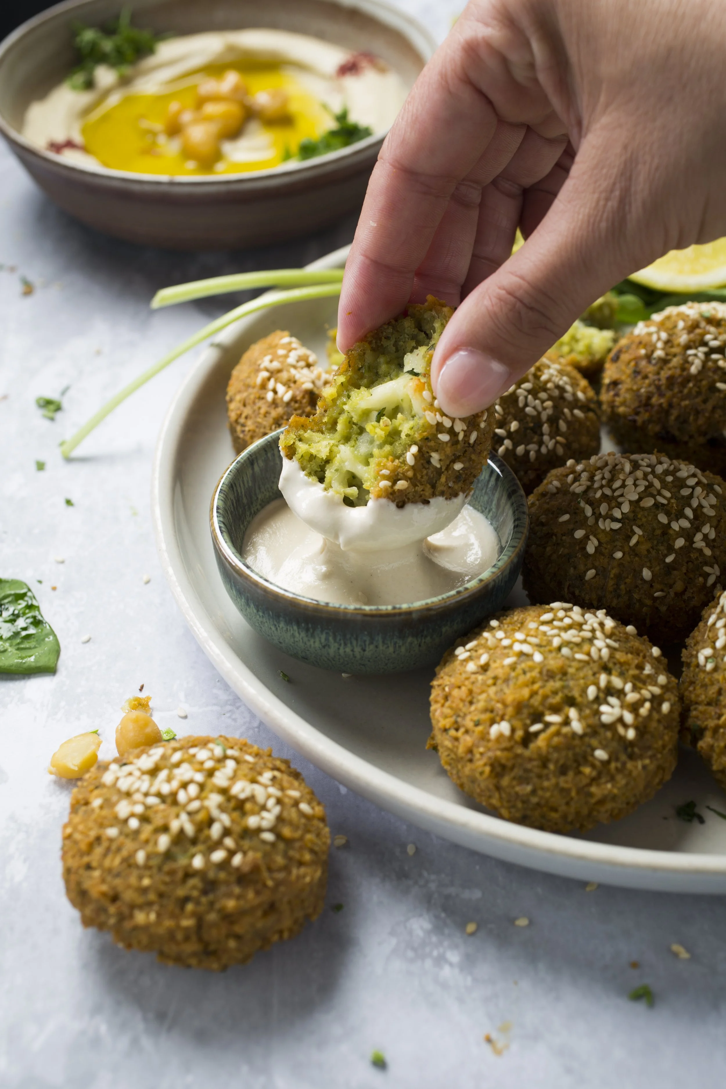 Person dipping a falafel ball into a bowl of creamy white sauce 
