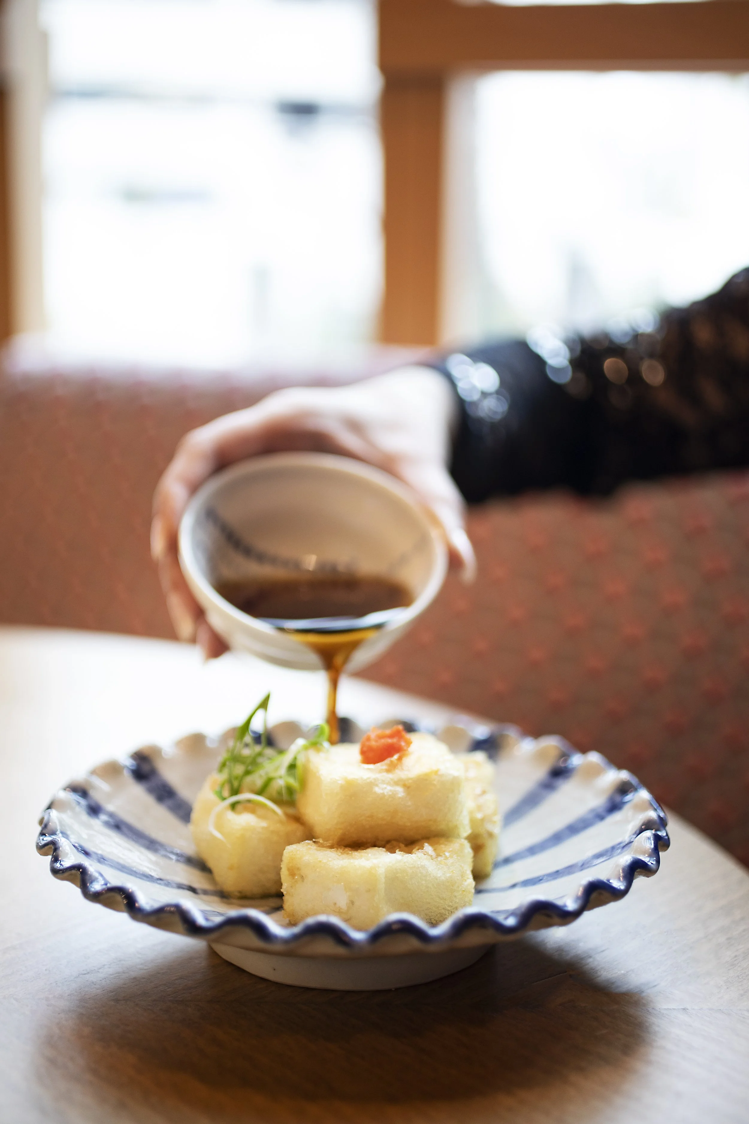 Person pouring soy sauce over Japanese tamagoyaki omelette on a decorative plate.