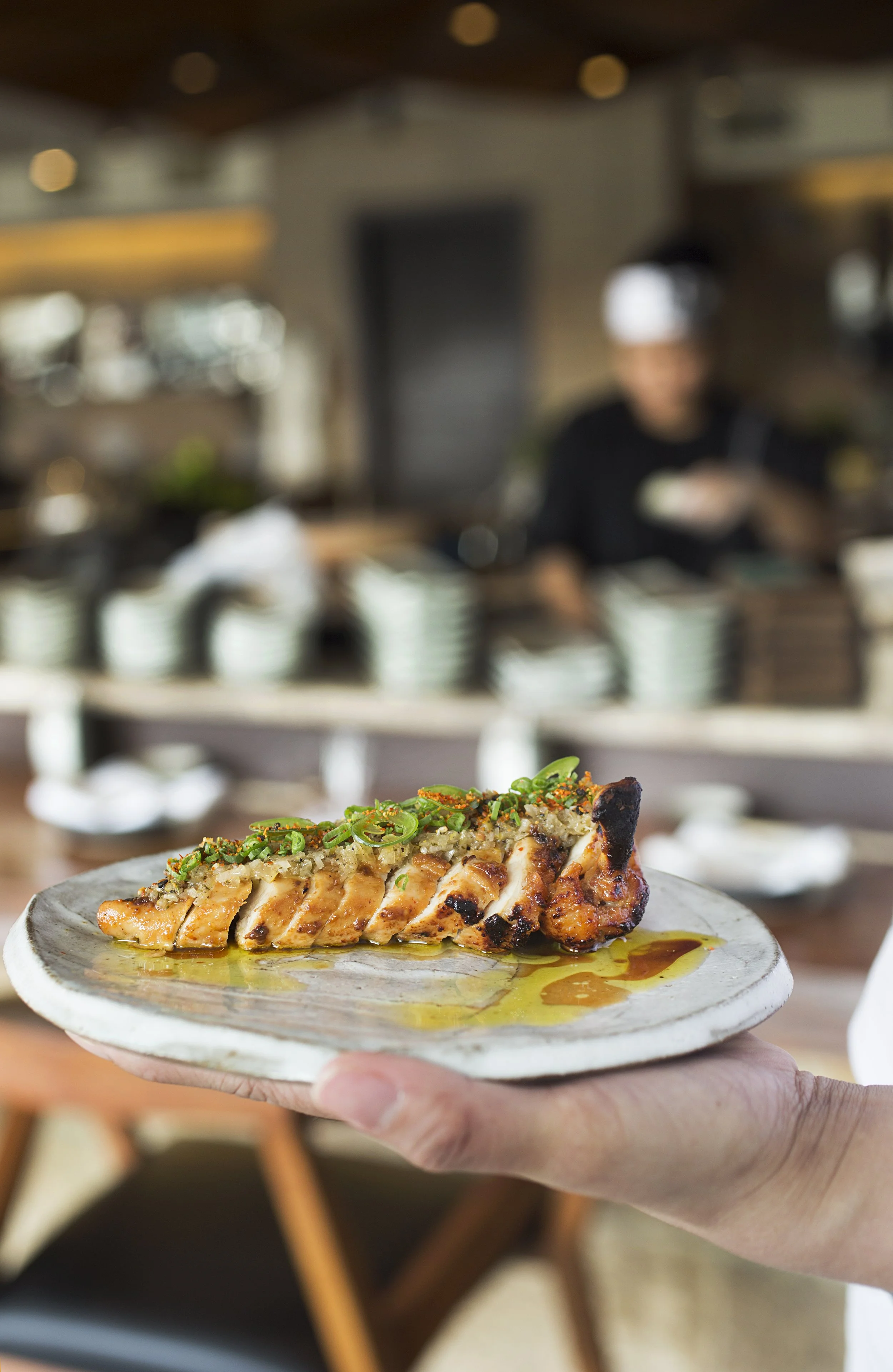 Close-up of a person holding plate with a grilled chicken piece drizzled with sauce