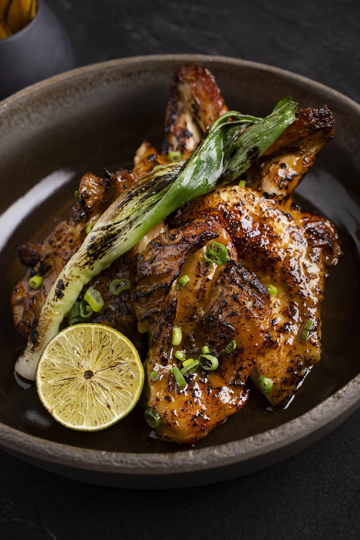 Grilled chicken thigh garnished with chopped green onions, a grilled green onion, a halved lime