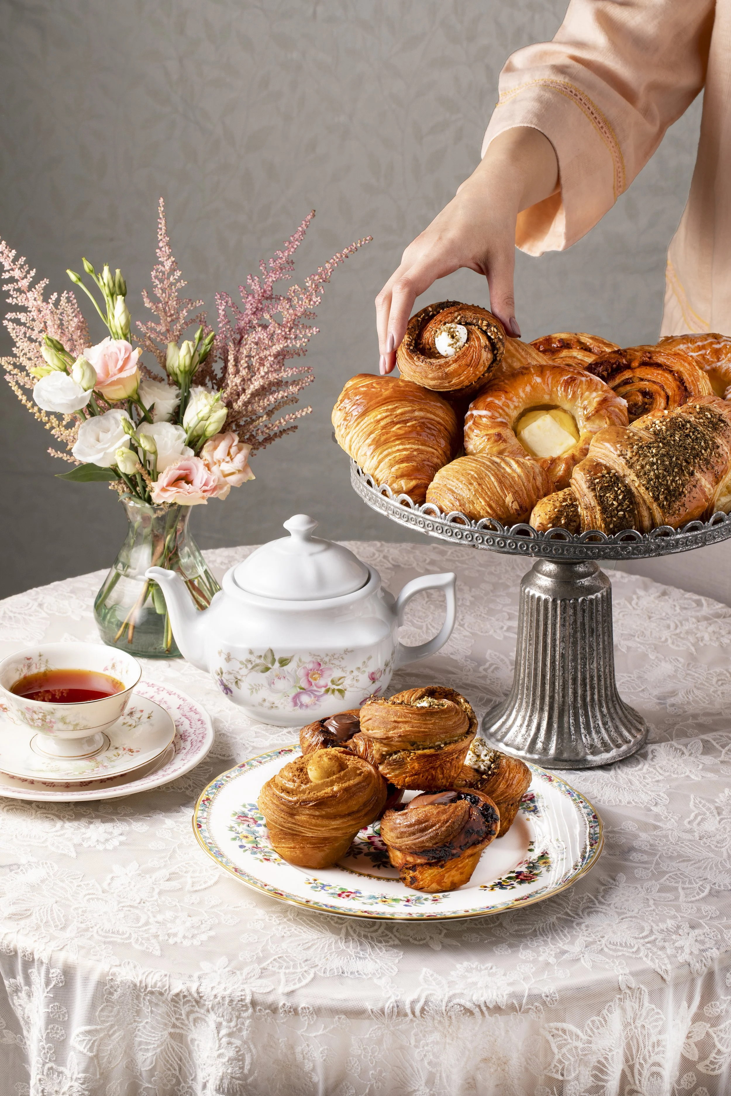 A person arranging an assortment of croissants and pastries on a silver cake stand 