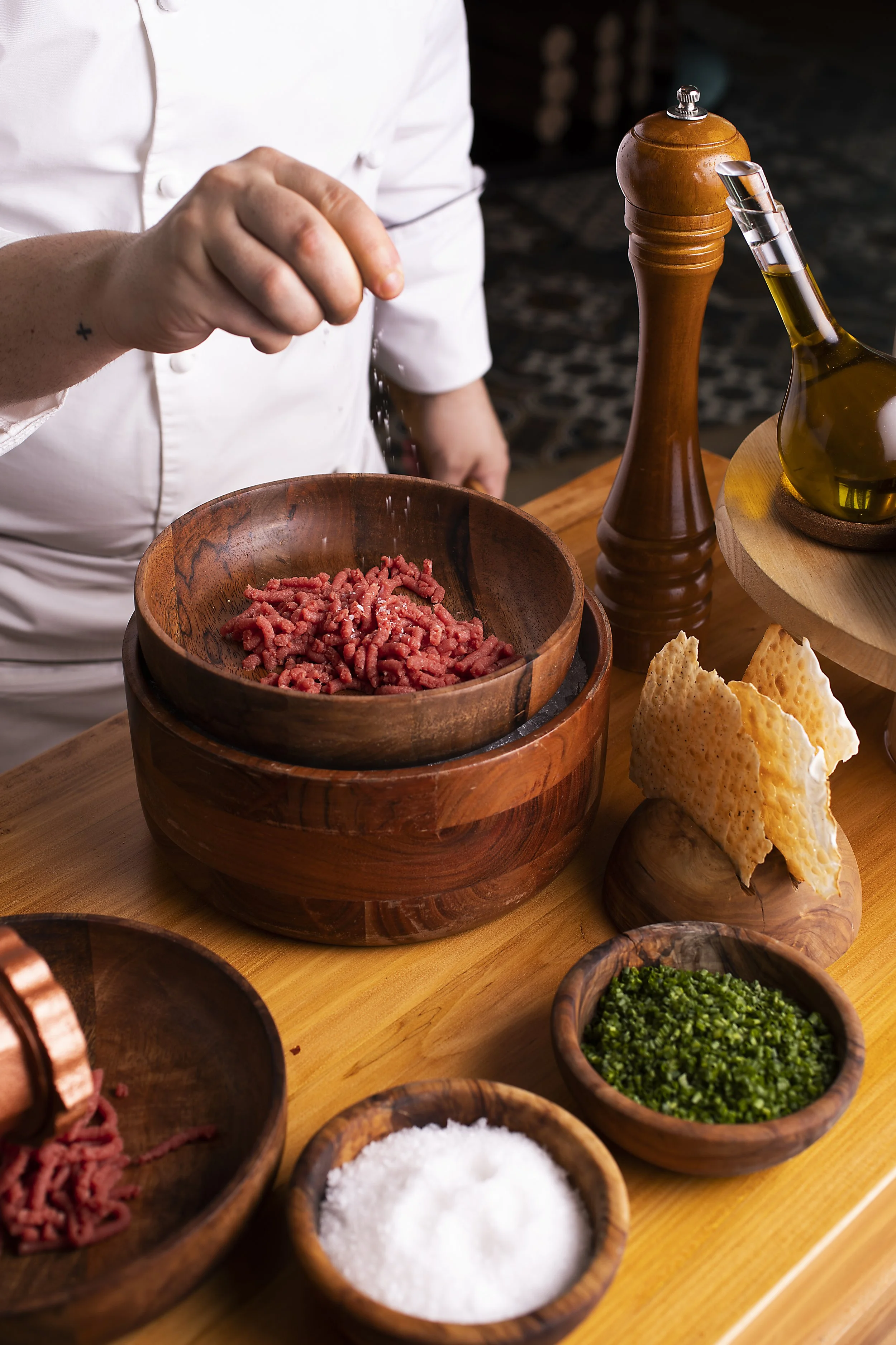 A chef seasoning ground beef with salt in a wooden bowl