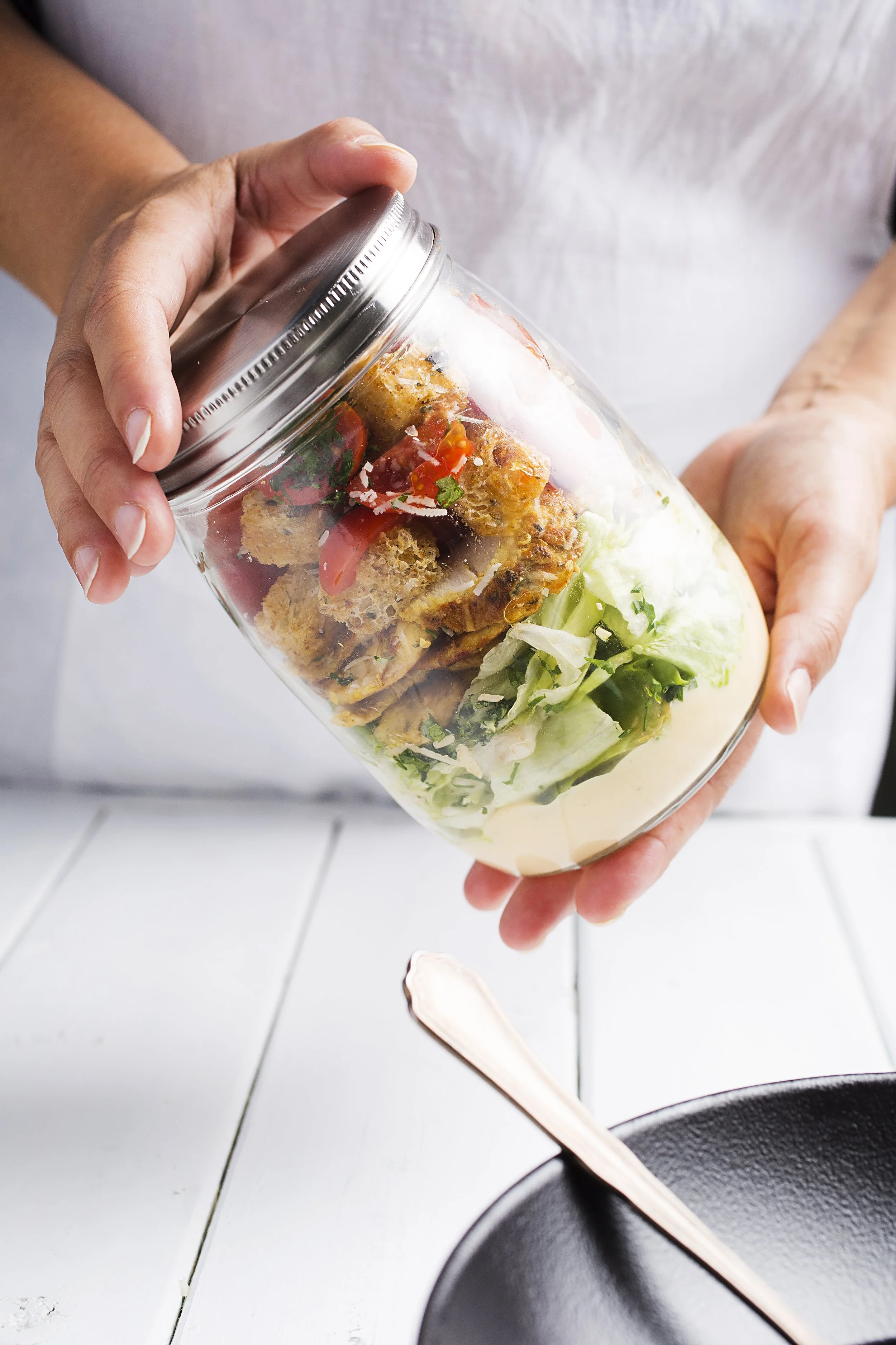 Person placing a glass jar filled with salad and croutons on a table.
