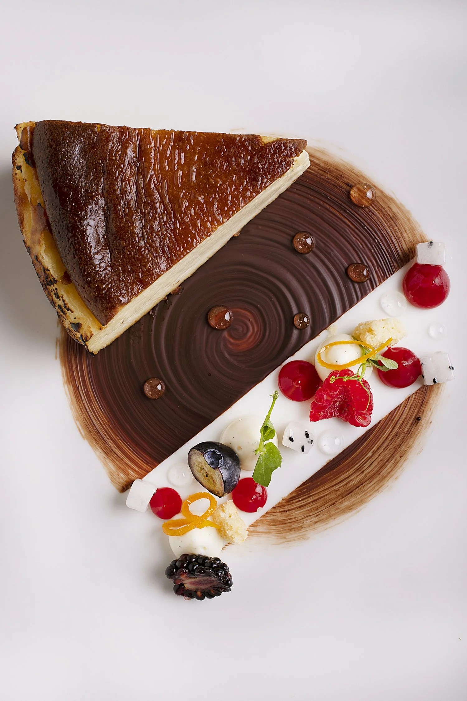 A slice of cheesecake with a graham cracker crust on a decorative plate with chocolate, berries, and edible garnishes. 