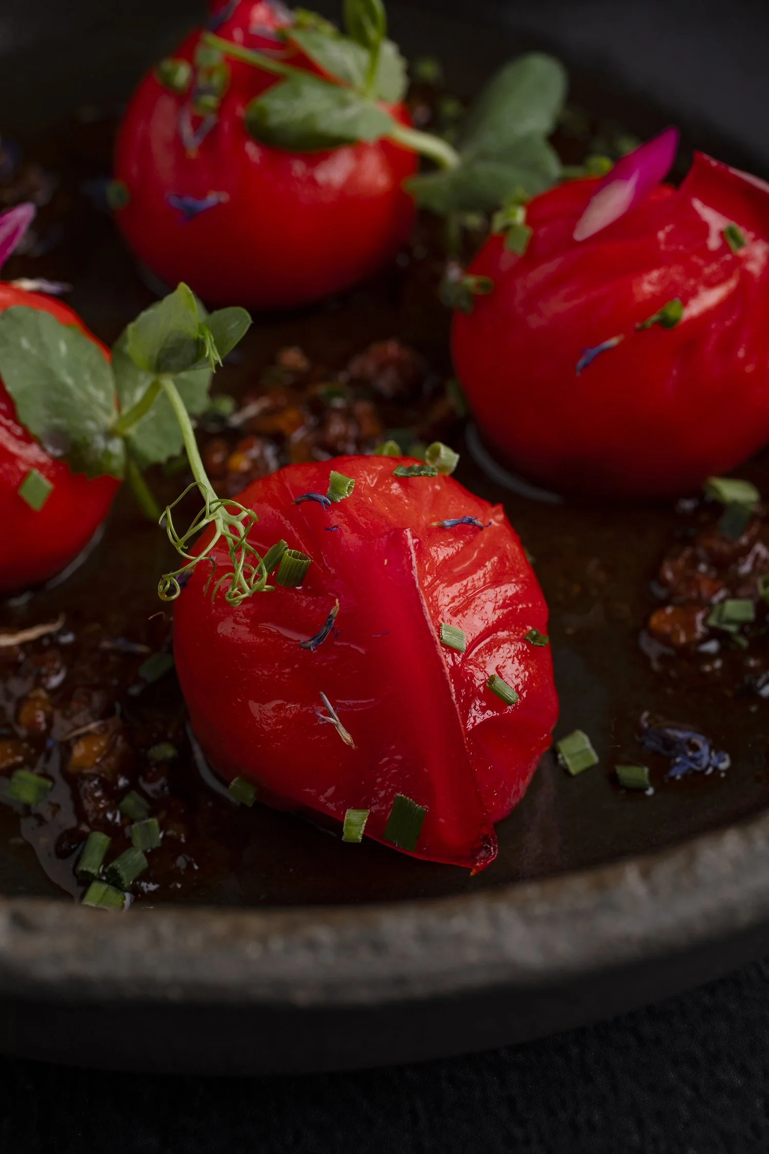 Roasted cherry tomatoes garnished with chopped chives and microgreens on a dark surface. 