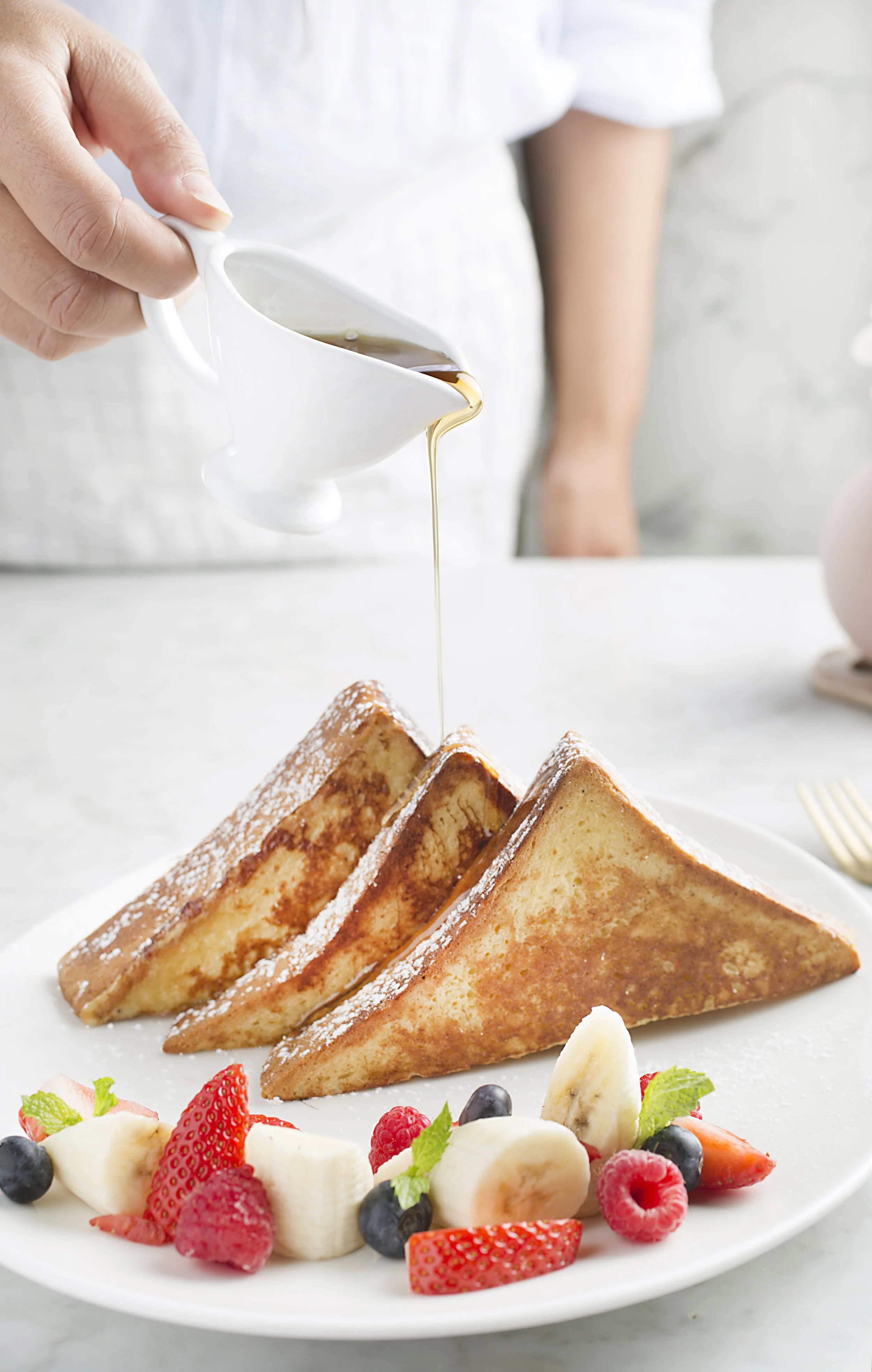 French toast with powdered sugar, topped with fresh strawberries, blueberries, bananas