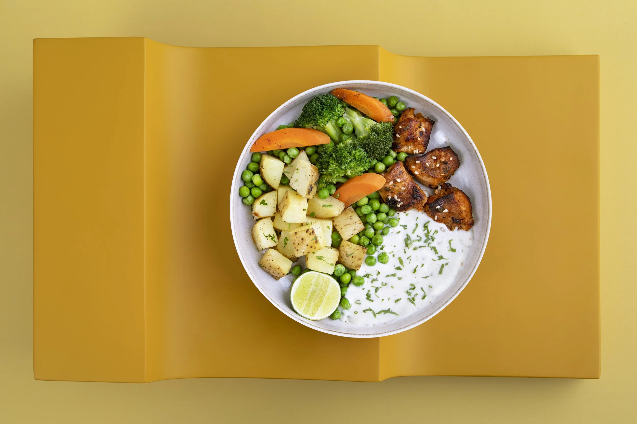 A bowl of grilled chicken, potatoes, broccoli, carrots, peas