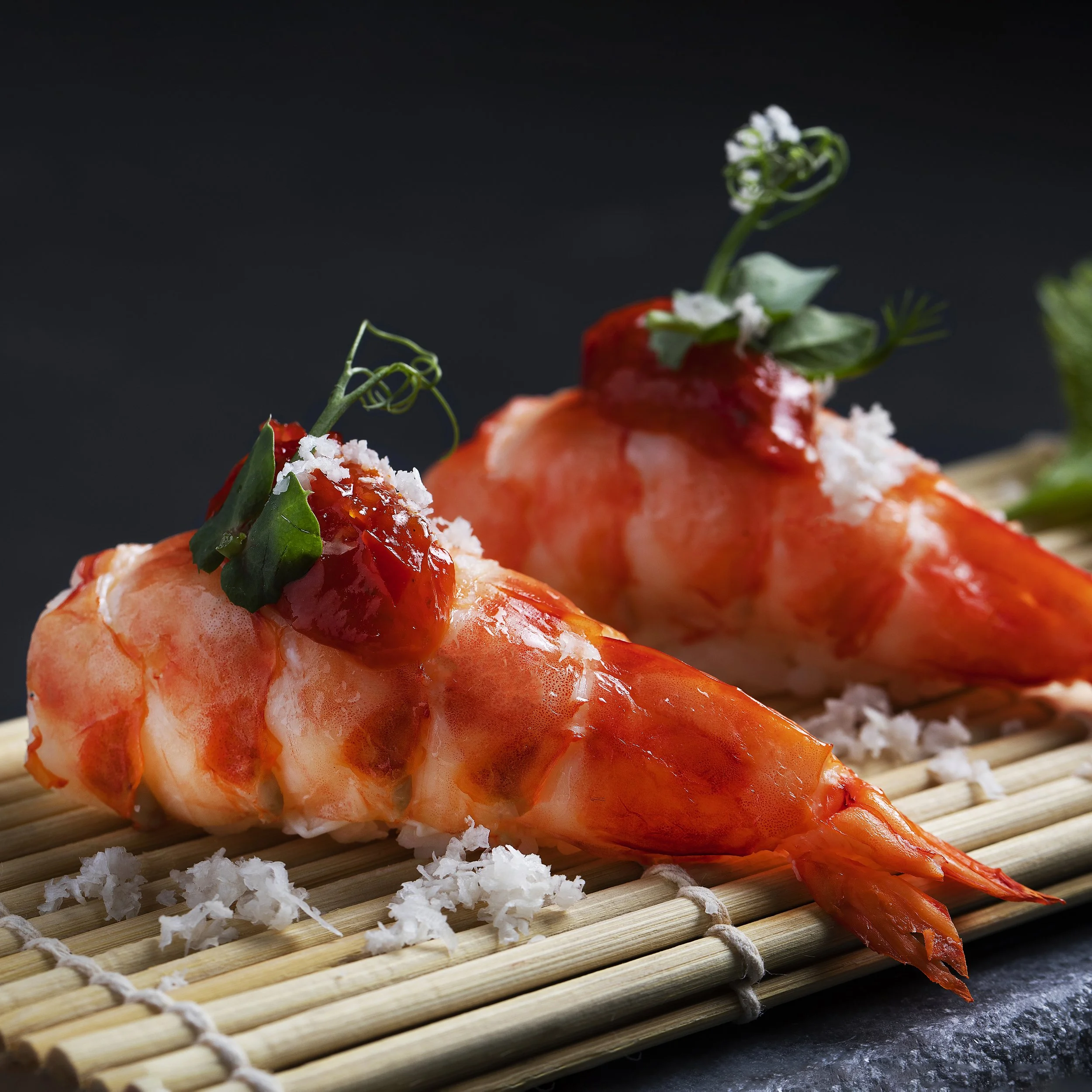 Close-up of two cooked shrimp topped with a dollop of red sauce, garnished with herbs