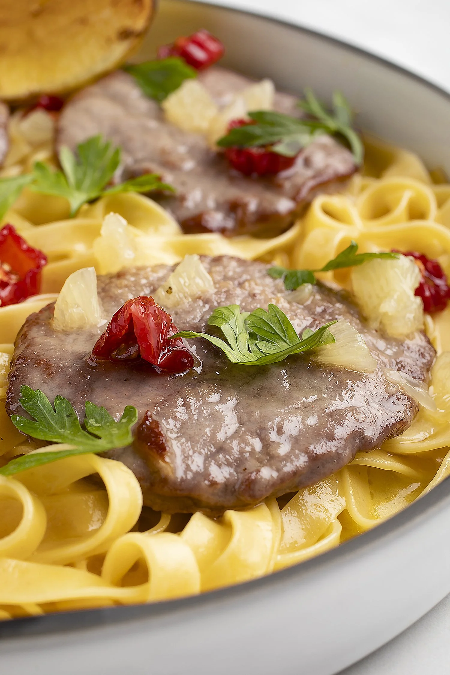 Pasta with meat sauce, garnished with parsley, chopped pineapple, and sun-dried tomatoes in a white bowl.