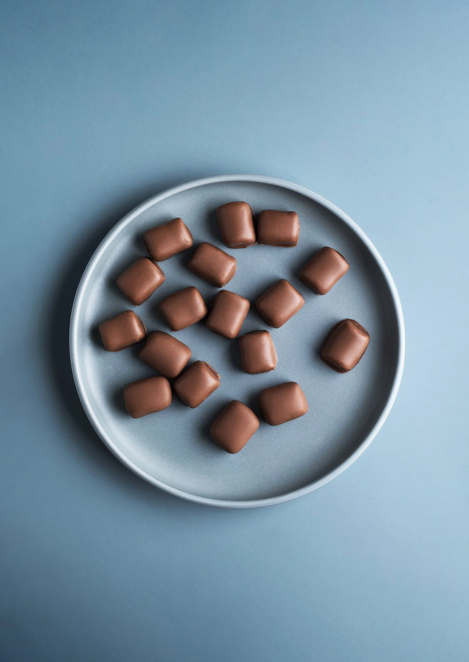 A blue plate with small, square-shaped chocolate candies on a matching blue background. 