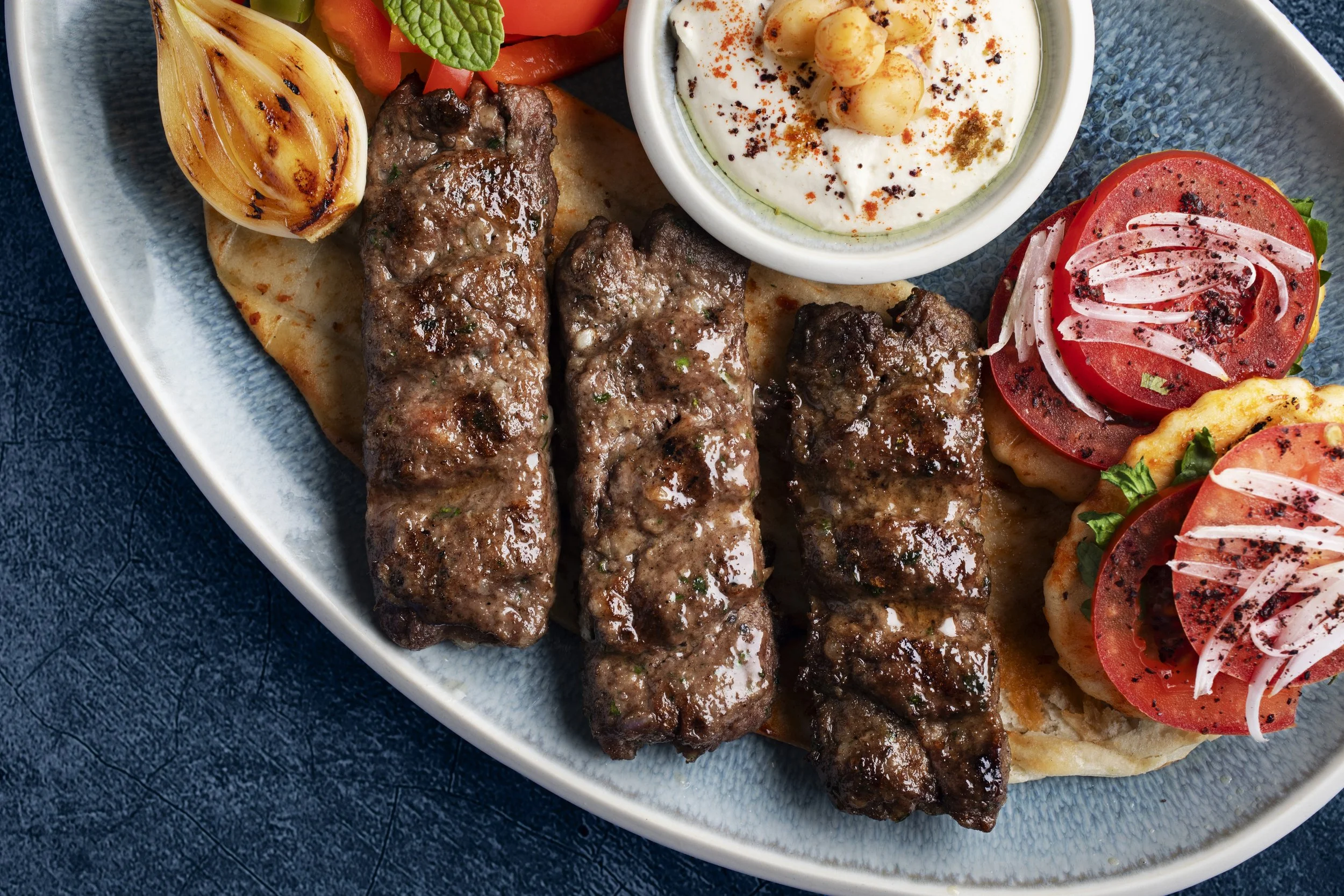 Plate of grilled kebabs with grilled vegetables, fresh tomato and onion salad