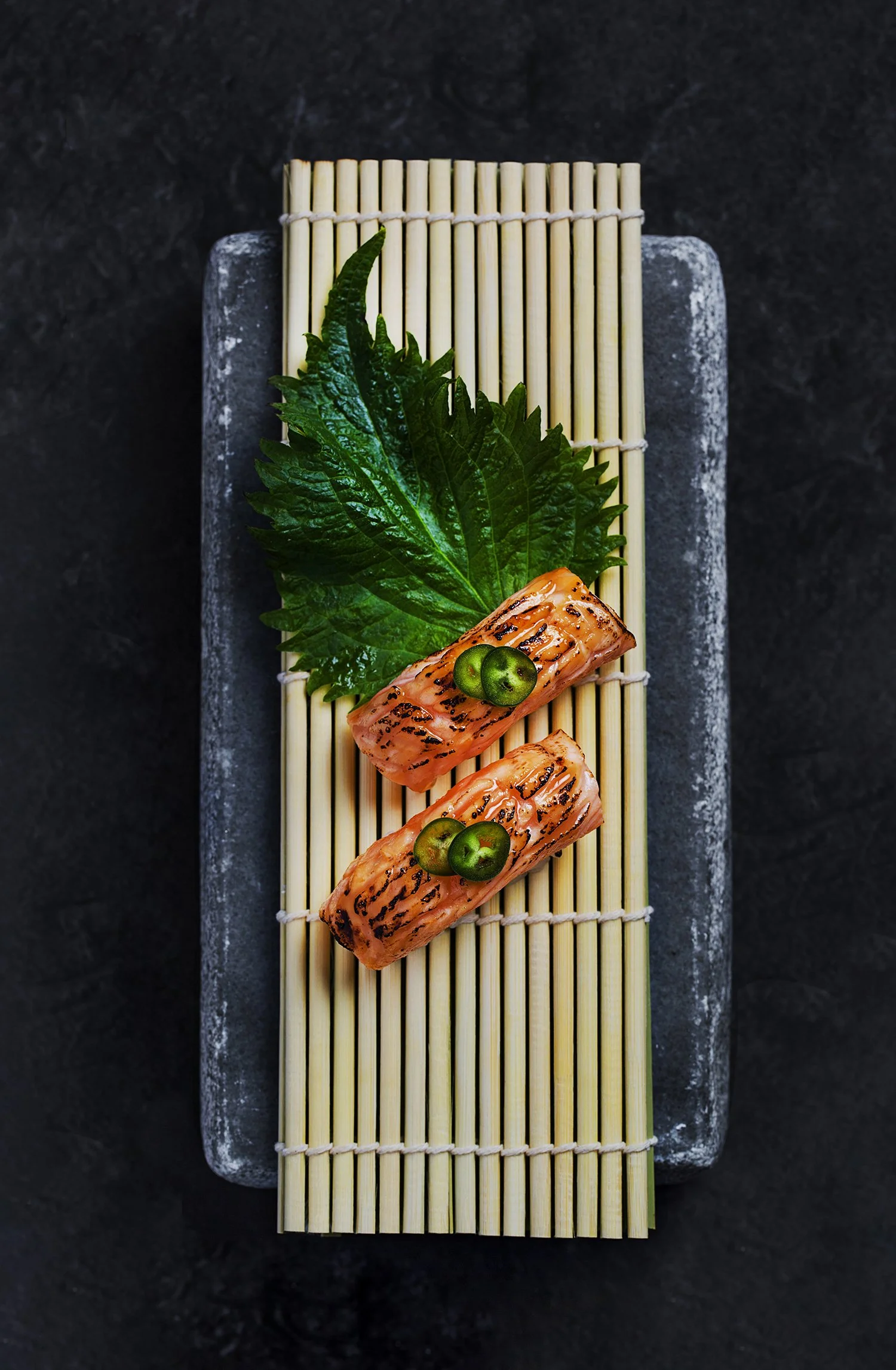 Grilled salmon slices garnished with green pepper and shiso leaf on sushi mat. Food photography in Kuwait