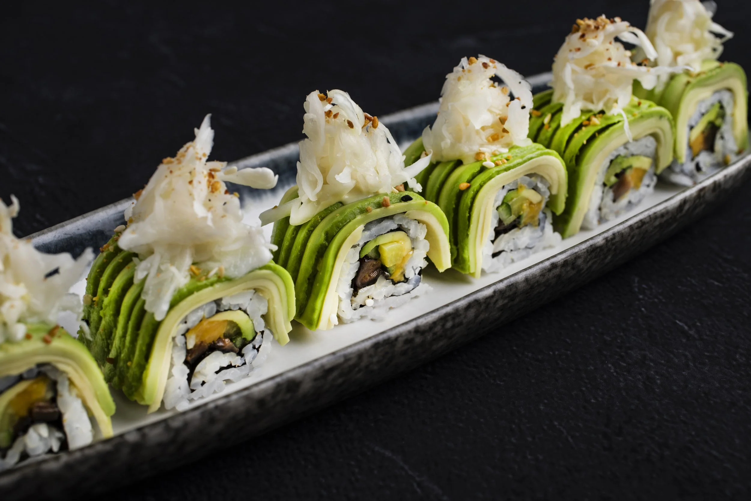 Sushi rolls topped with shredded white fish and sesame seeds, arranged on a rectangular ceramic plate.