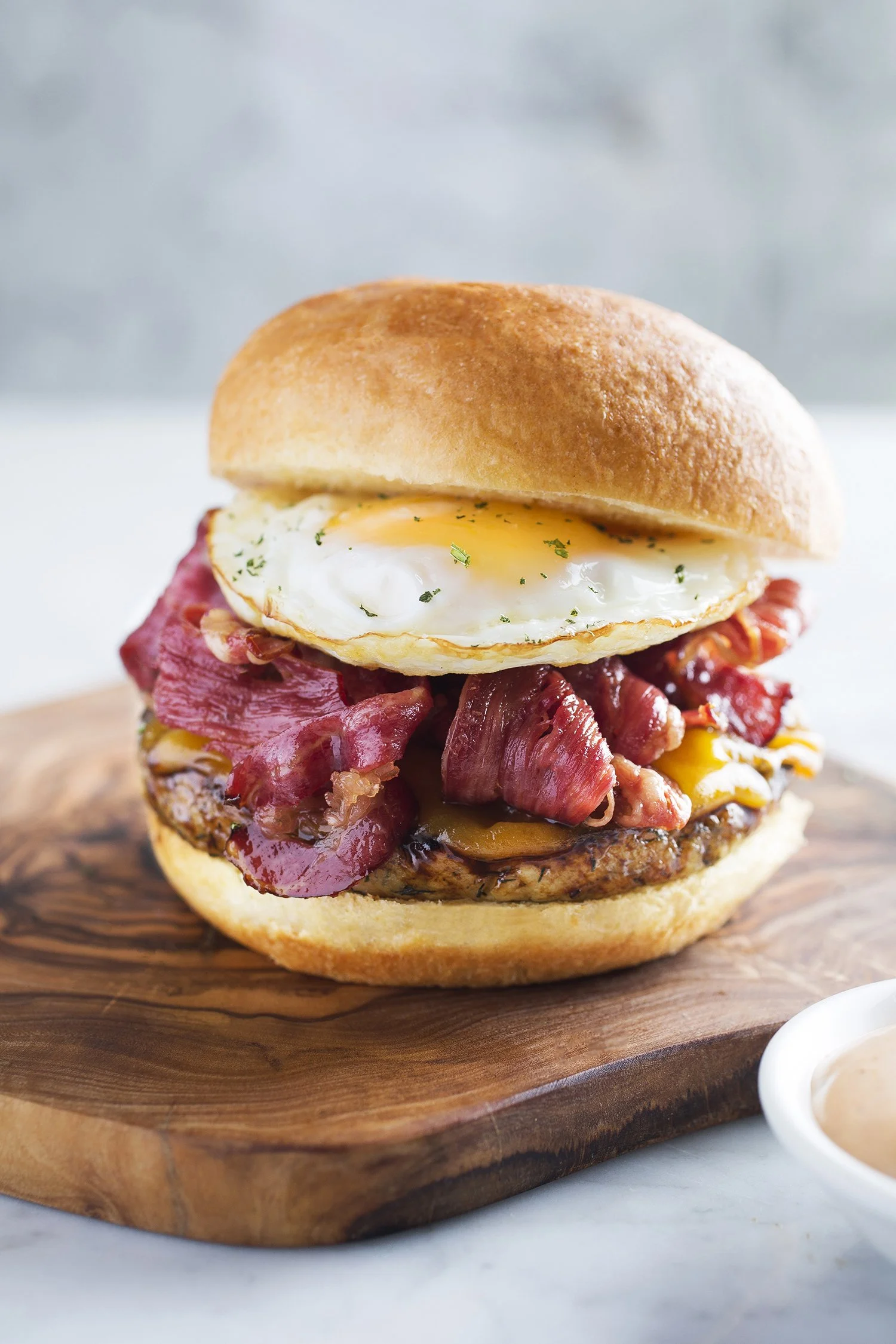 A breakfast burger with a fried egg, bacon, cheese, on a bun, served on a wooden board. 