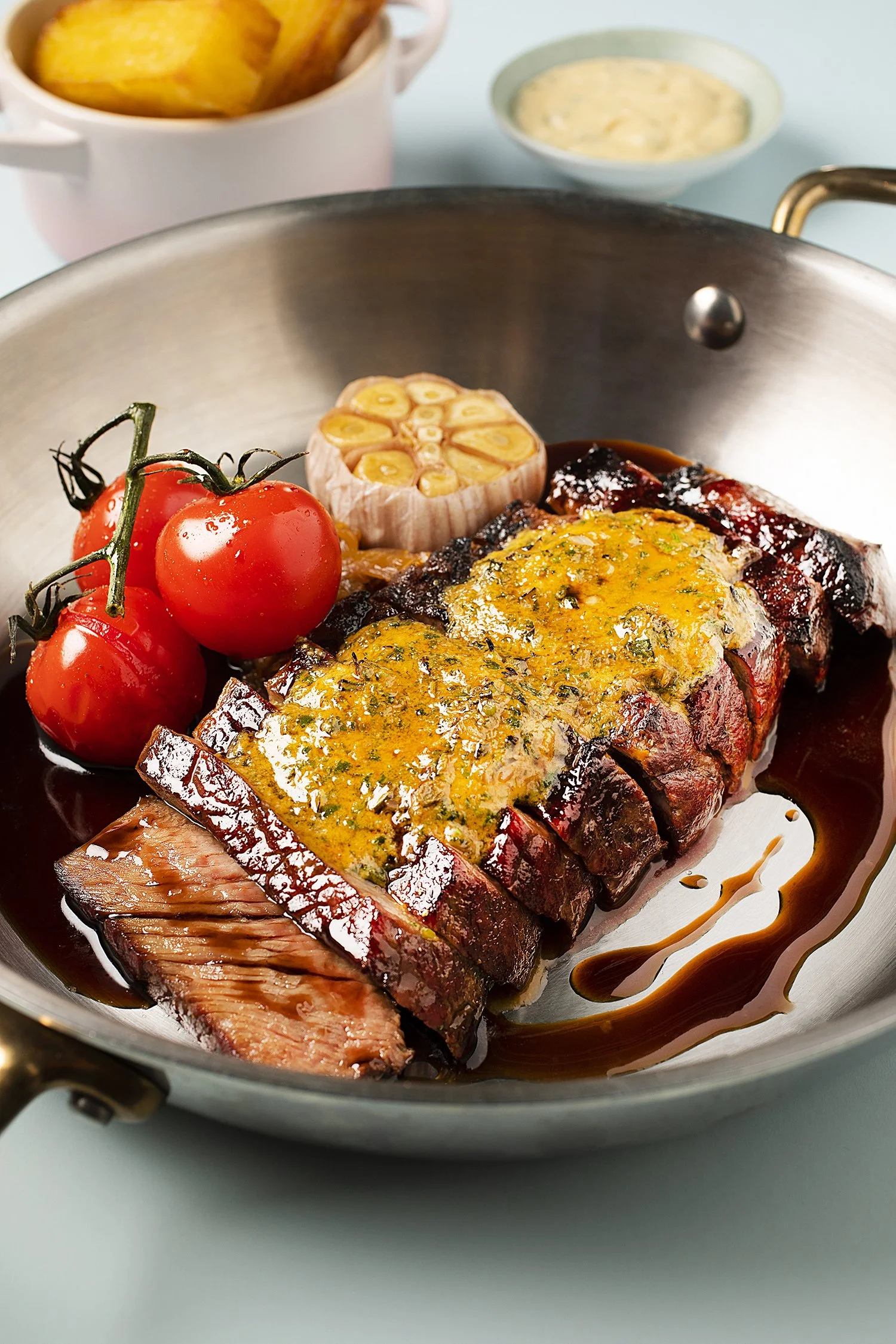 Slice of cooked steak with herbs, cherry tomatoes, and roasted garlic in a pan