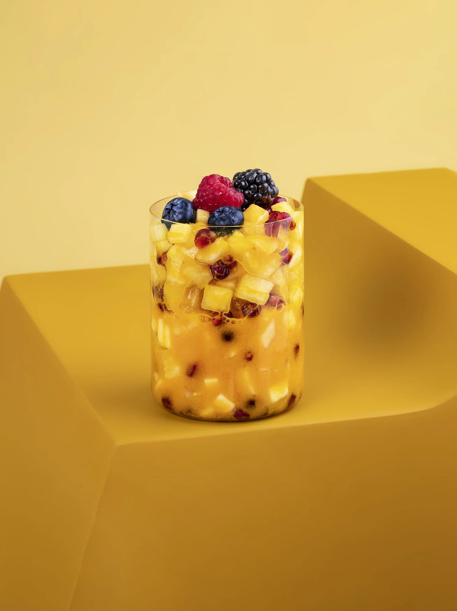 A tall glass filled with diced fruit, topped with fresh berries