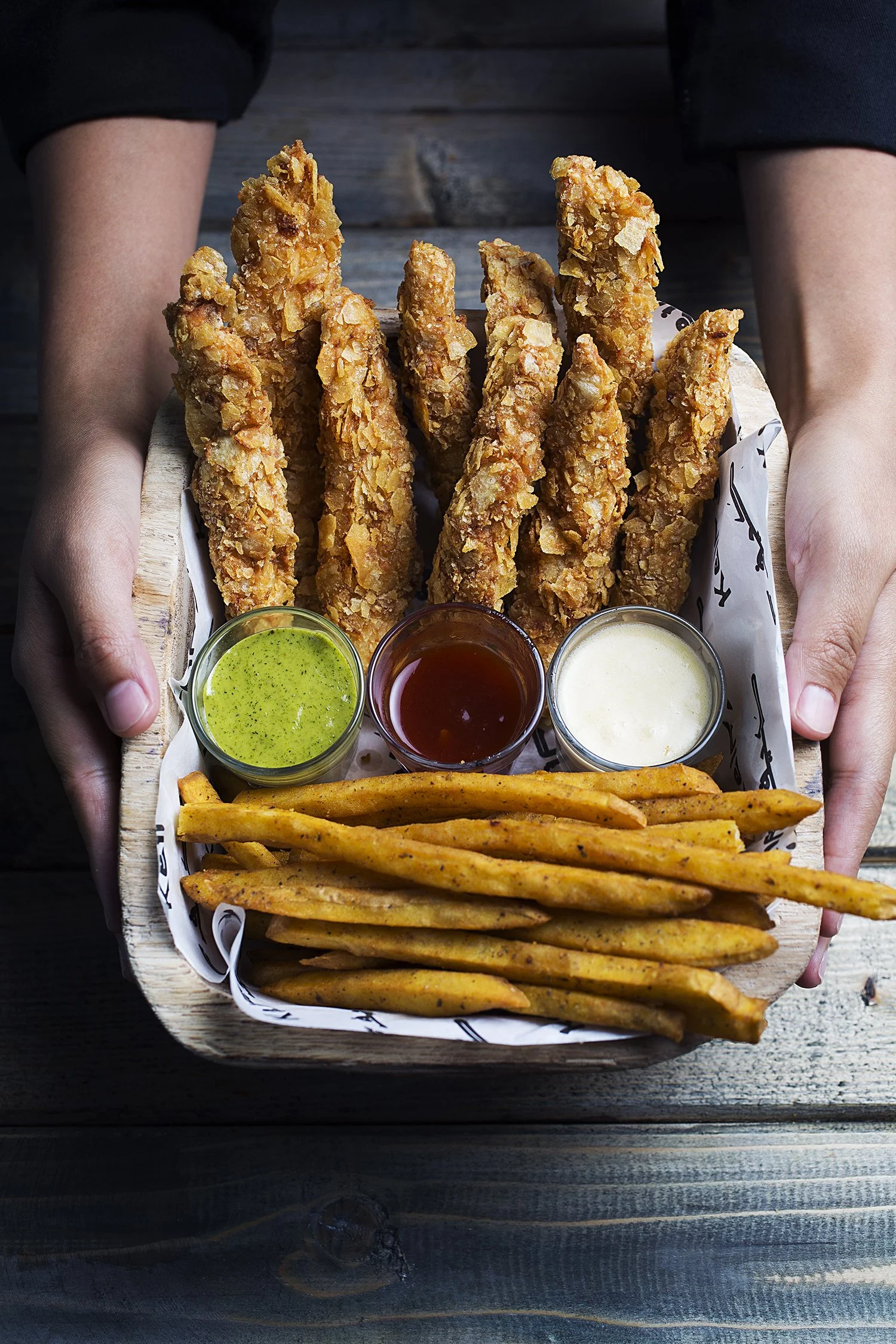 A basket of fried chicken tenders with three dipping sauces, served with seasoned French fries. 