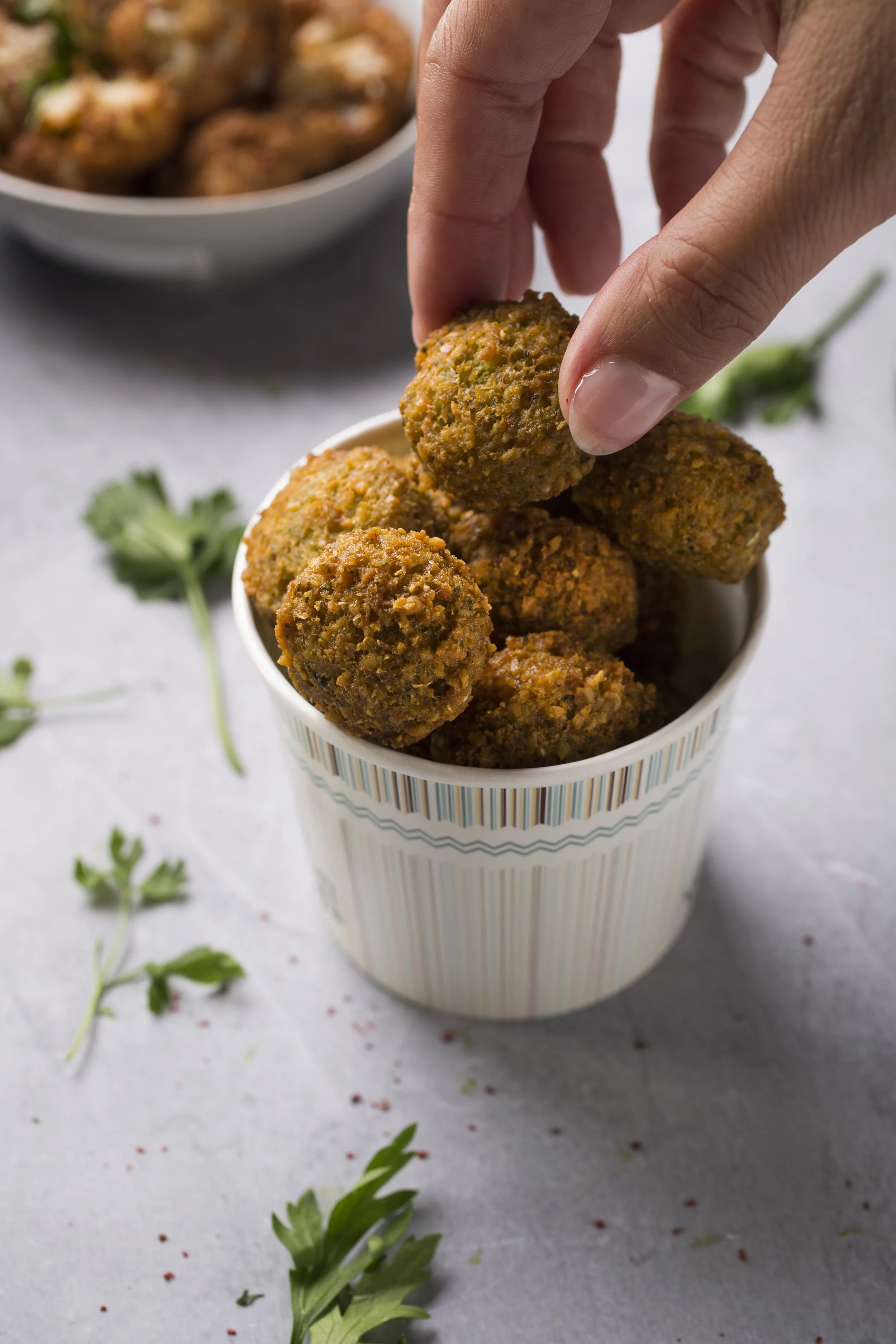 A hand holding a falafel over a paper cup 
