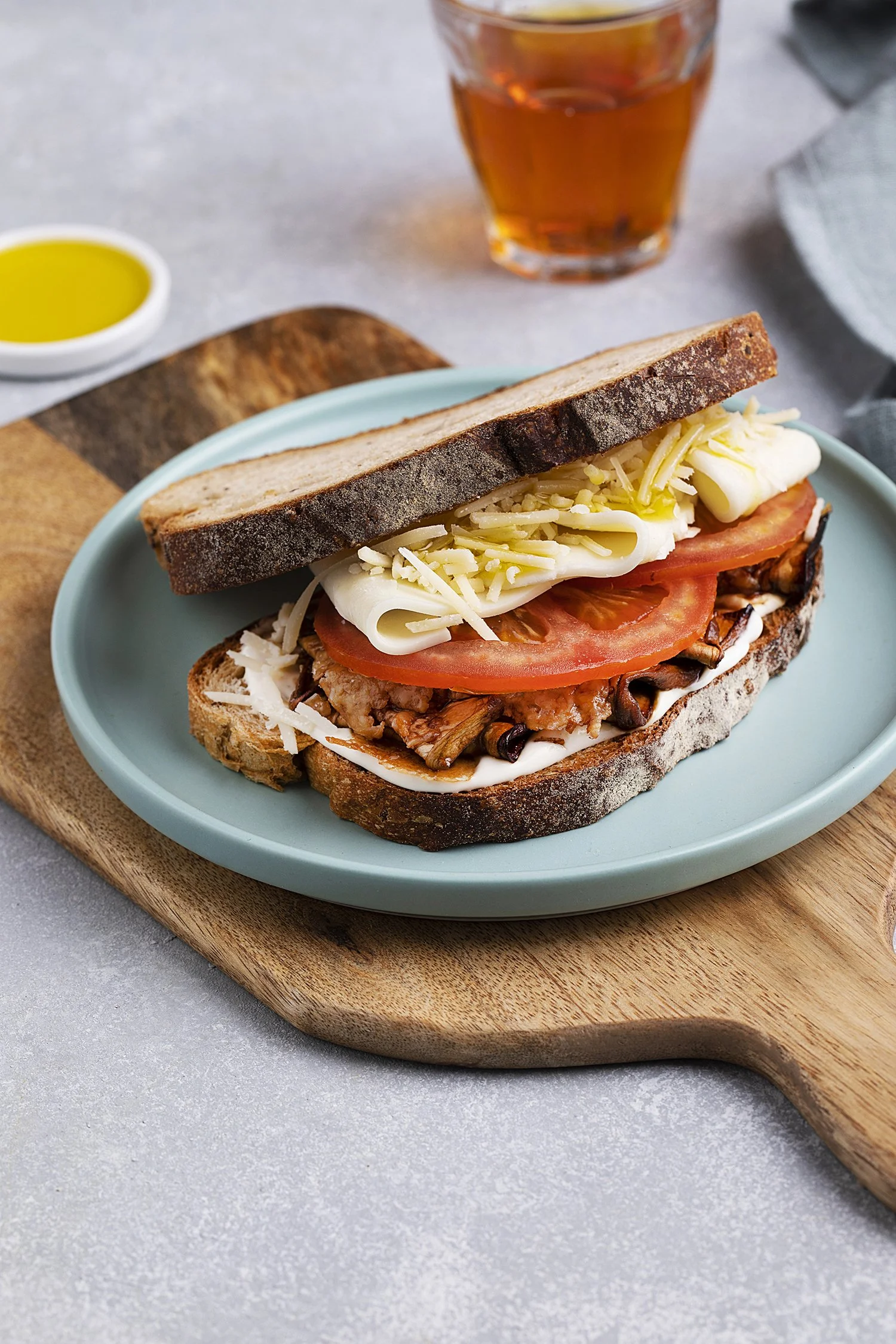 A sandwich on a light blue plate with toasted bread, cheese, tomato, mushrooms, and meat, Menu shoot for Numou