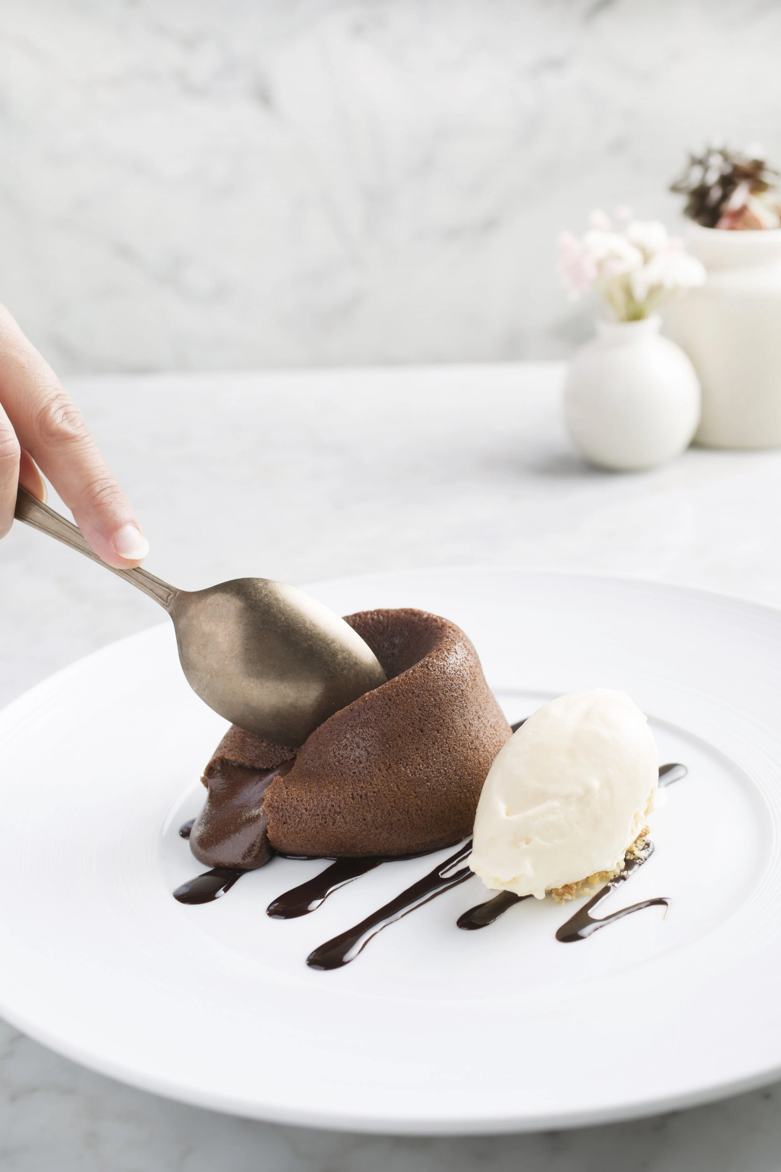 Chocolate lava cake with a scoop of vanilla ice cream on a white plate, garnished with chocolate sauce.