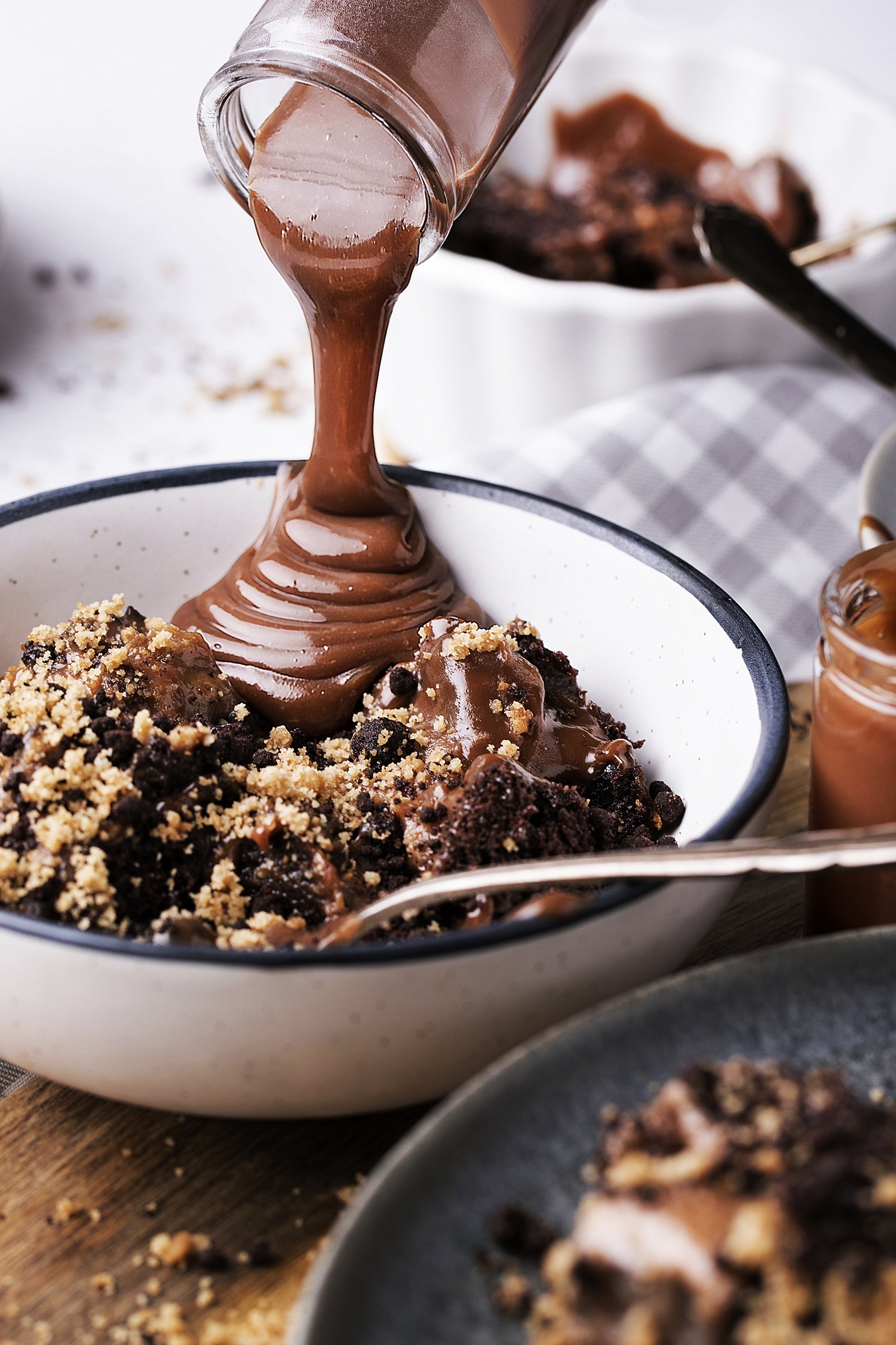 Chocolate brownie topped with chocolate pudding and crumbles, with chocolate sauce being poured over it. 
