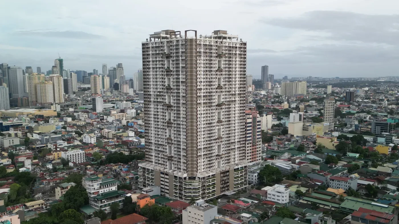 A tall high-rise building in a cityscape with numerous smaller buildings and skyscrapers in the background under a partly cloudy sky.