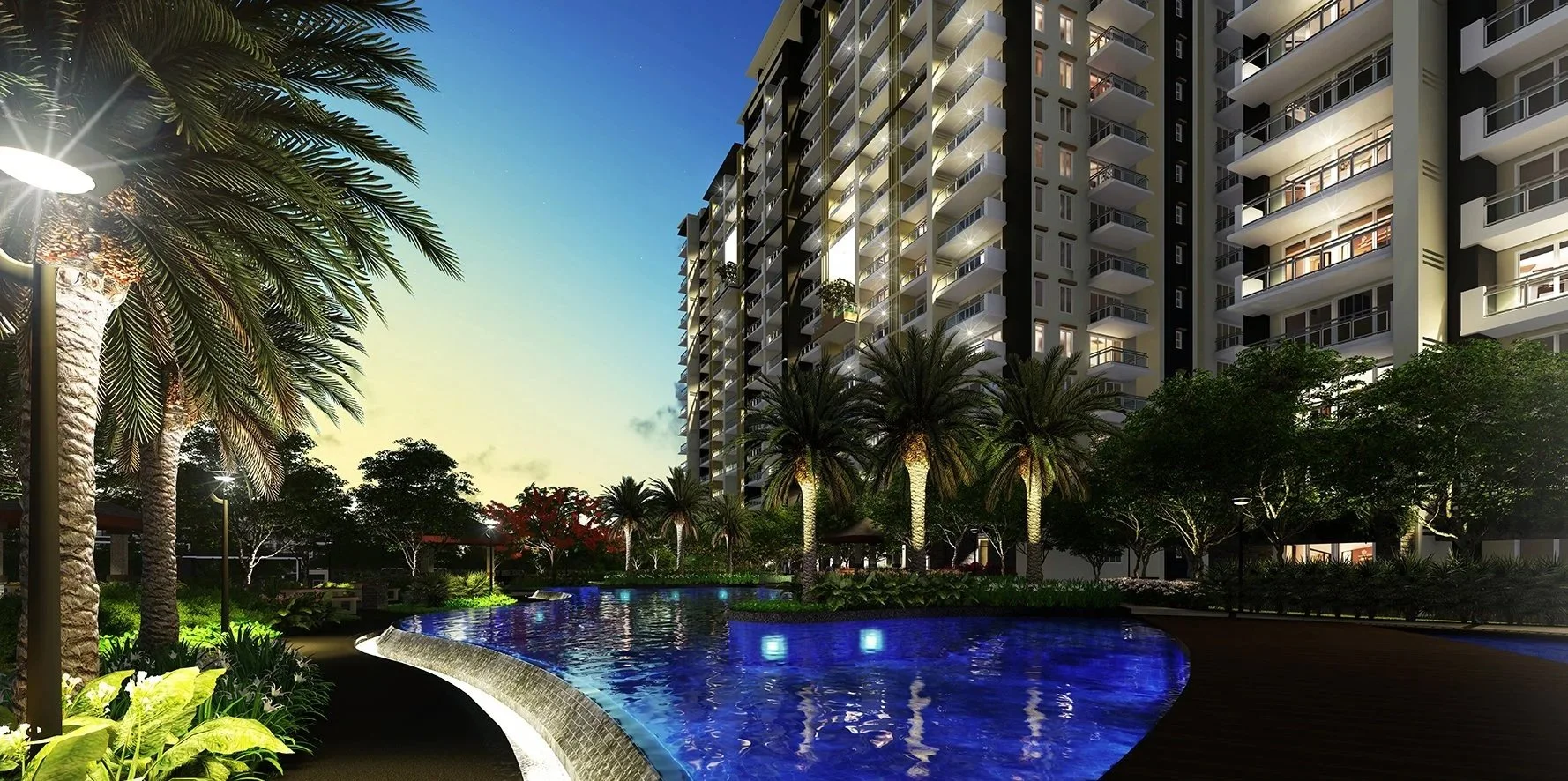 Nighttime view of a luxurious residential complex with a swimming pool, tall palm trees, and lush greenery, illuminated by outdoor lighting.