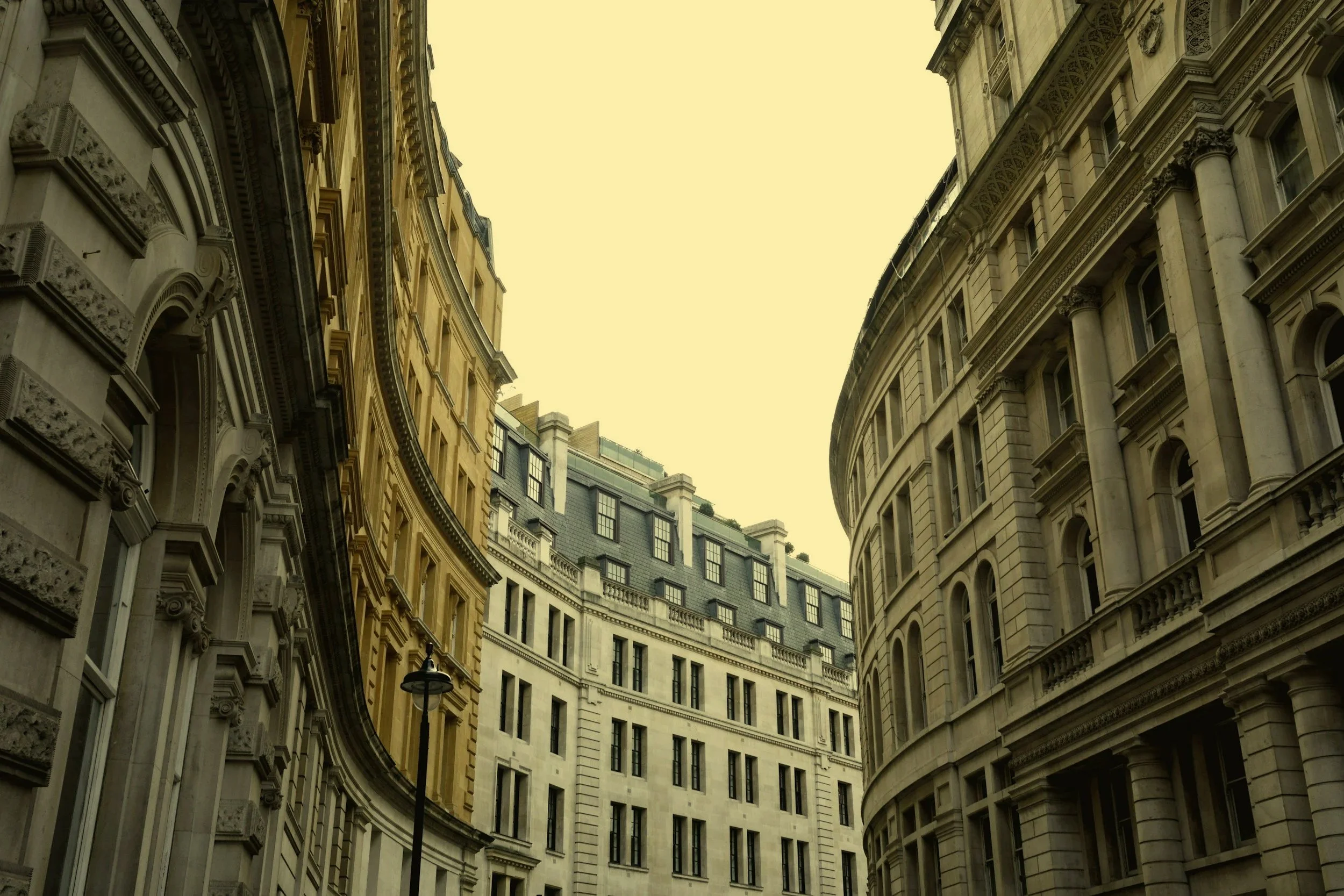 View of historic European-style buildings with ornate architectural details, curved facades, and multiple windows under a cloudy sky.