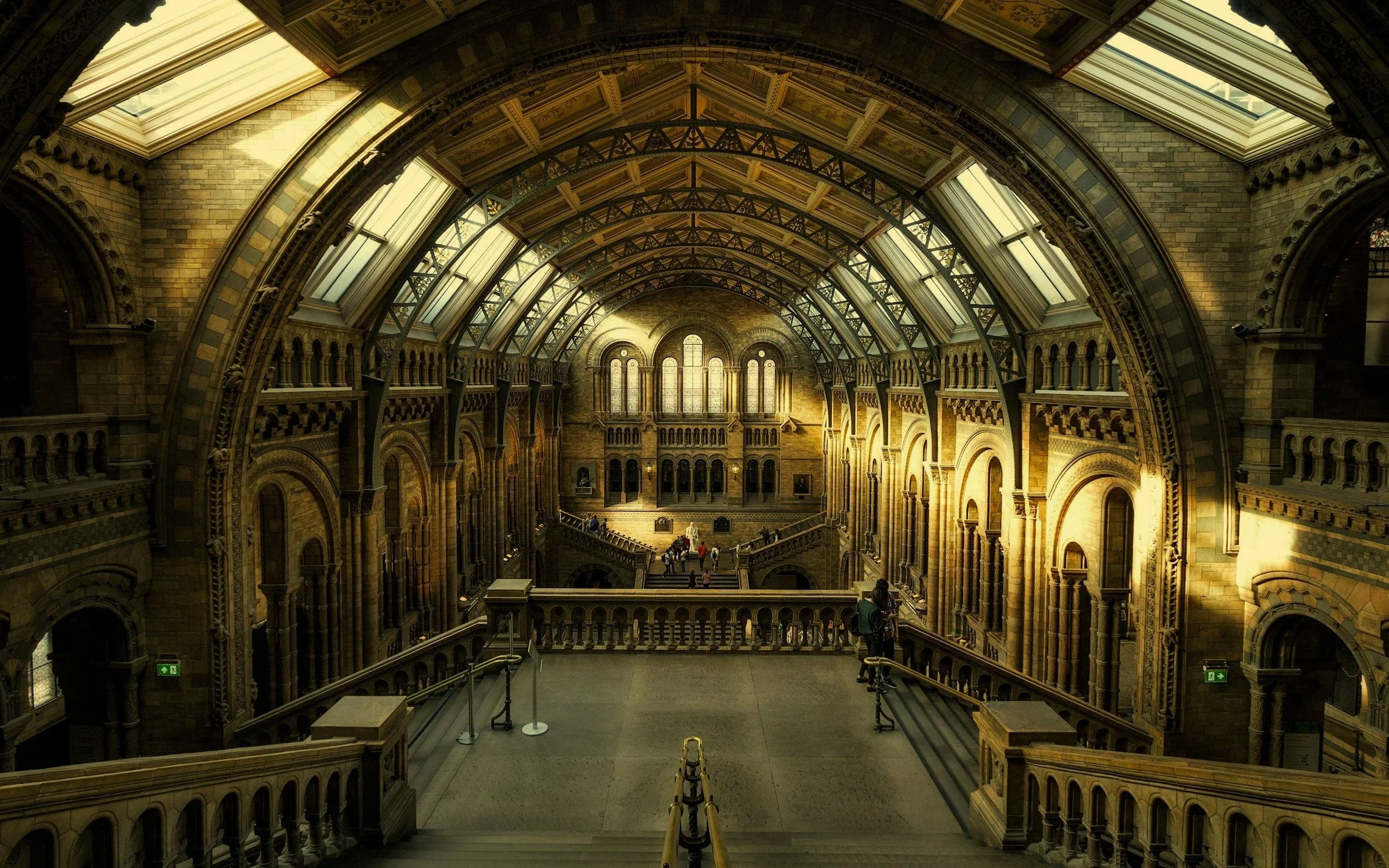 Interior view of a historic train station or grand hall with arched ceilings, large windows, and ornate architectural details. People are walking and standing on the upper level.