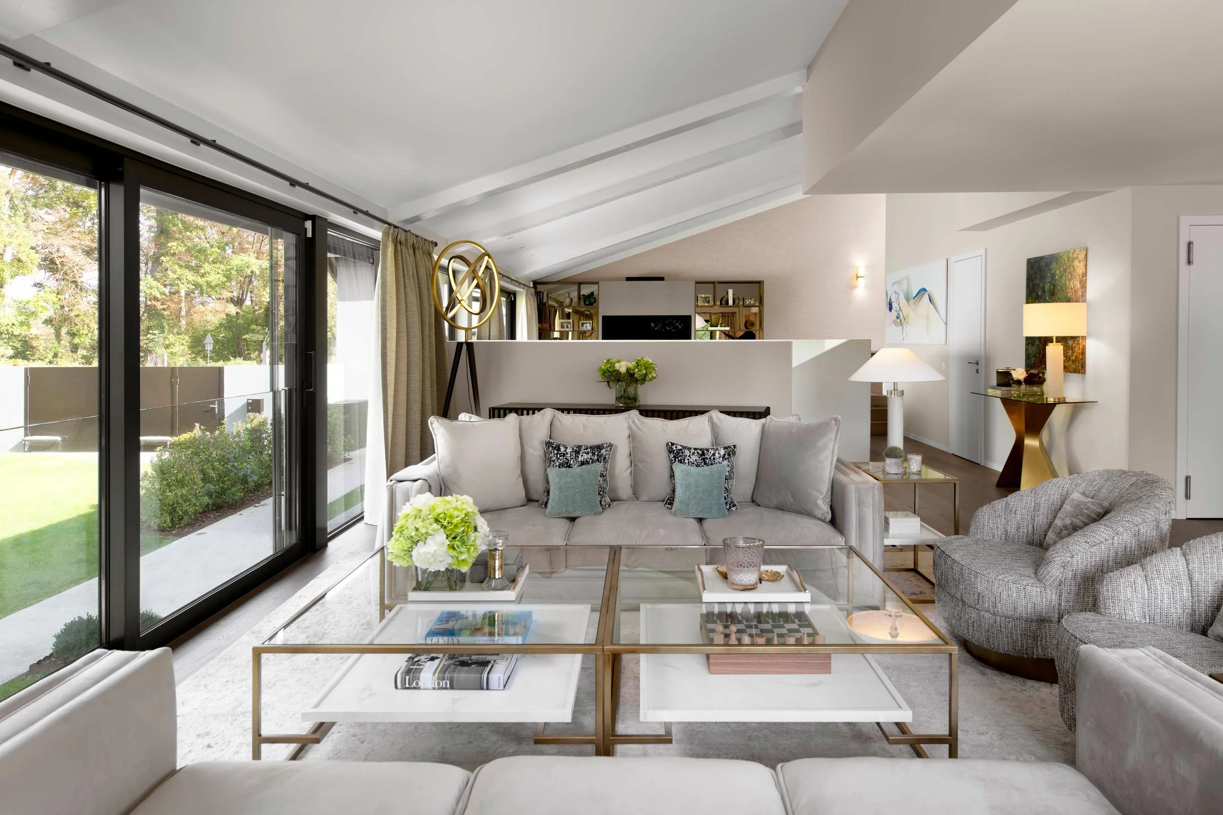 Living room with a white sofa, glass coffee table, armchair, side tables, decorative items, large sliding glass door, and garden view