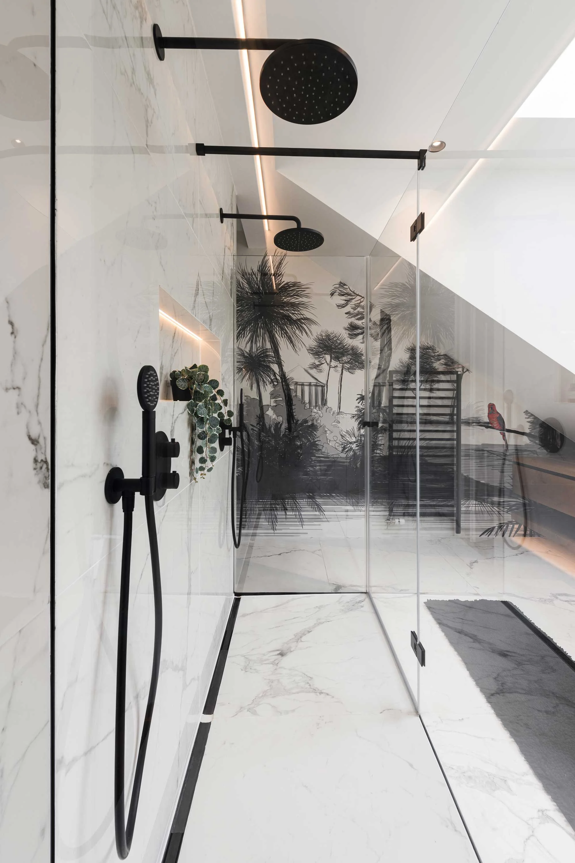 Modern walk-in shower with black fixtures and a glass partition, featuring a black and white jungle mural on the back wall.