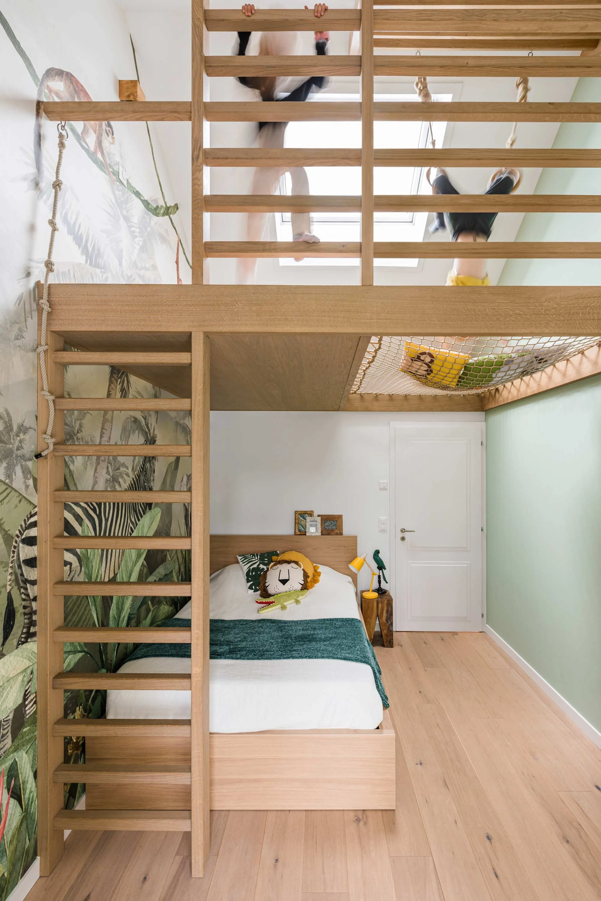 Boys Bedroom with a loft bed, featuring a jungle-themed wallpaper, a bed with plush toys, and children playing on the upper level.