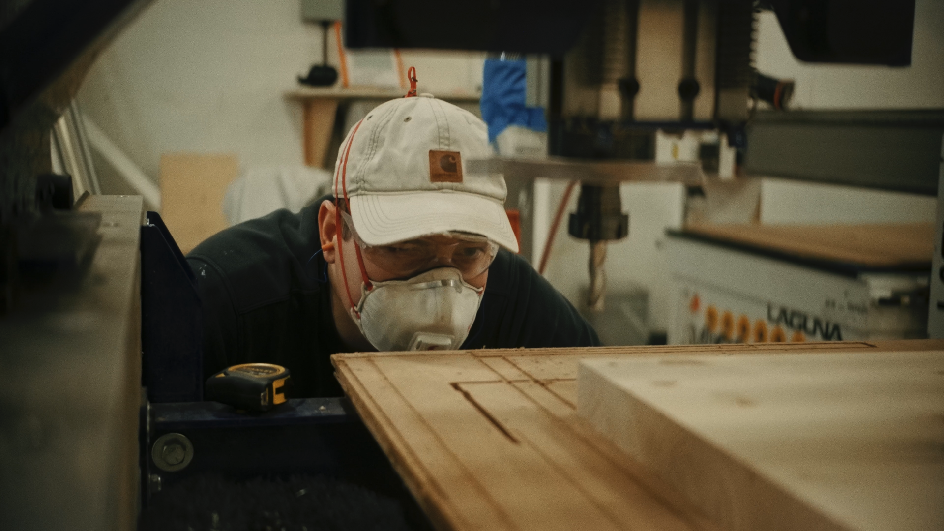 Person wearing black gloves is installing a glass top on a wooden table with a wooden frame and metal legs. The table has a decorative natural wood edge and an artistic resin surface underneath the glass.