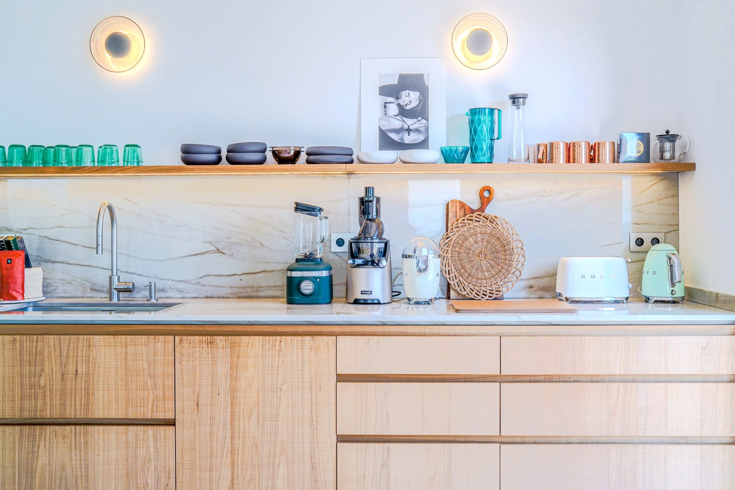 Cuisine moderne avec un plan de travail en marbre, nombreux appareils électroménagers pastel et accessoires en bois, affichant un décor épuré et lumineux.
