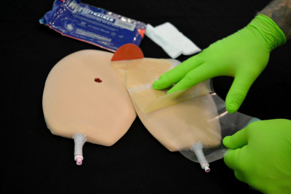 Gloved hands applying a chest seal to a realistic chest wound trainer