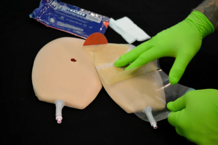Gloved hands applying a chest seal to a realistic chest wound trainer