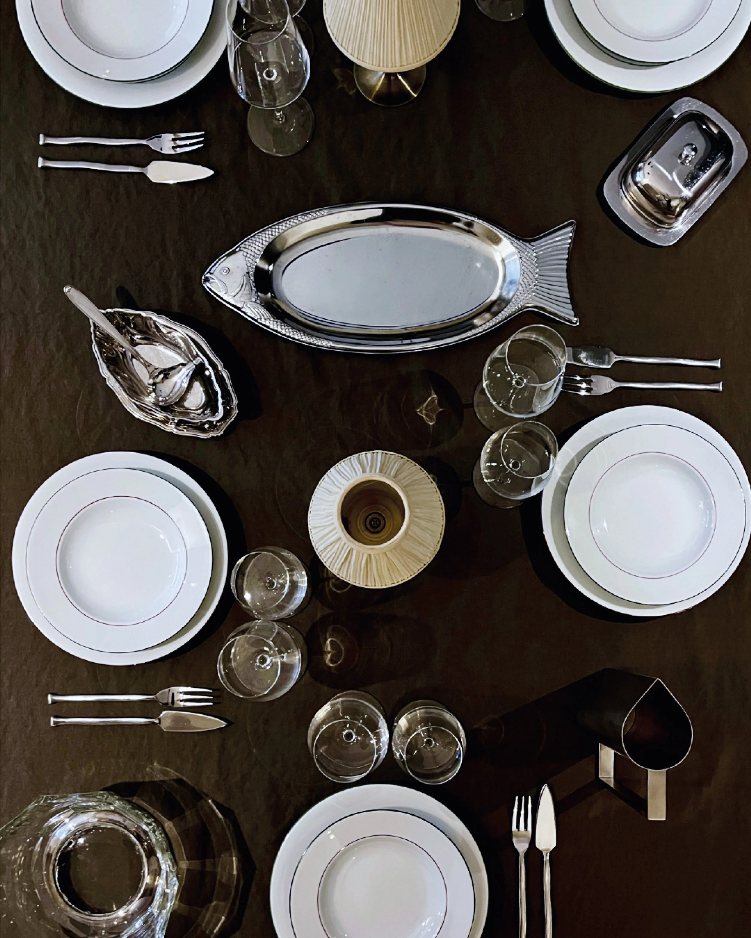 Table élégante dressée pour un repas, avec assiettes blanches, verres à vin, couverts en argent, et une assiette en forme de poisson en métal.