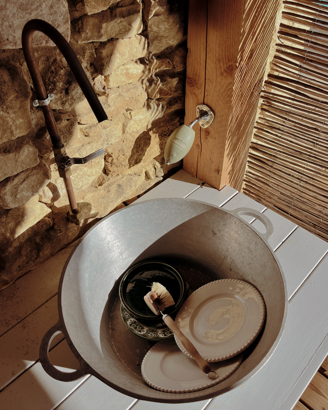 Evier extérieur en cuivre blanc avec des assiettes en céramique et un pinceau à vaisselle, à côté d'un évier en pierre .