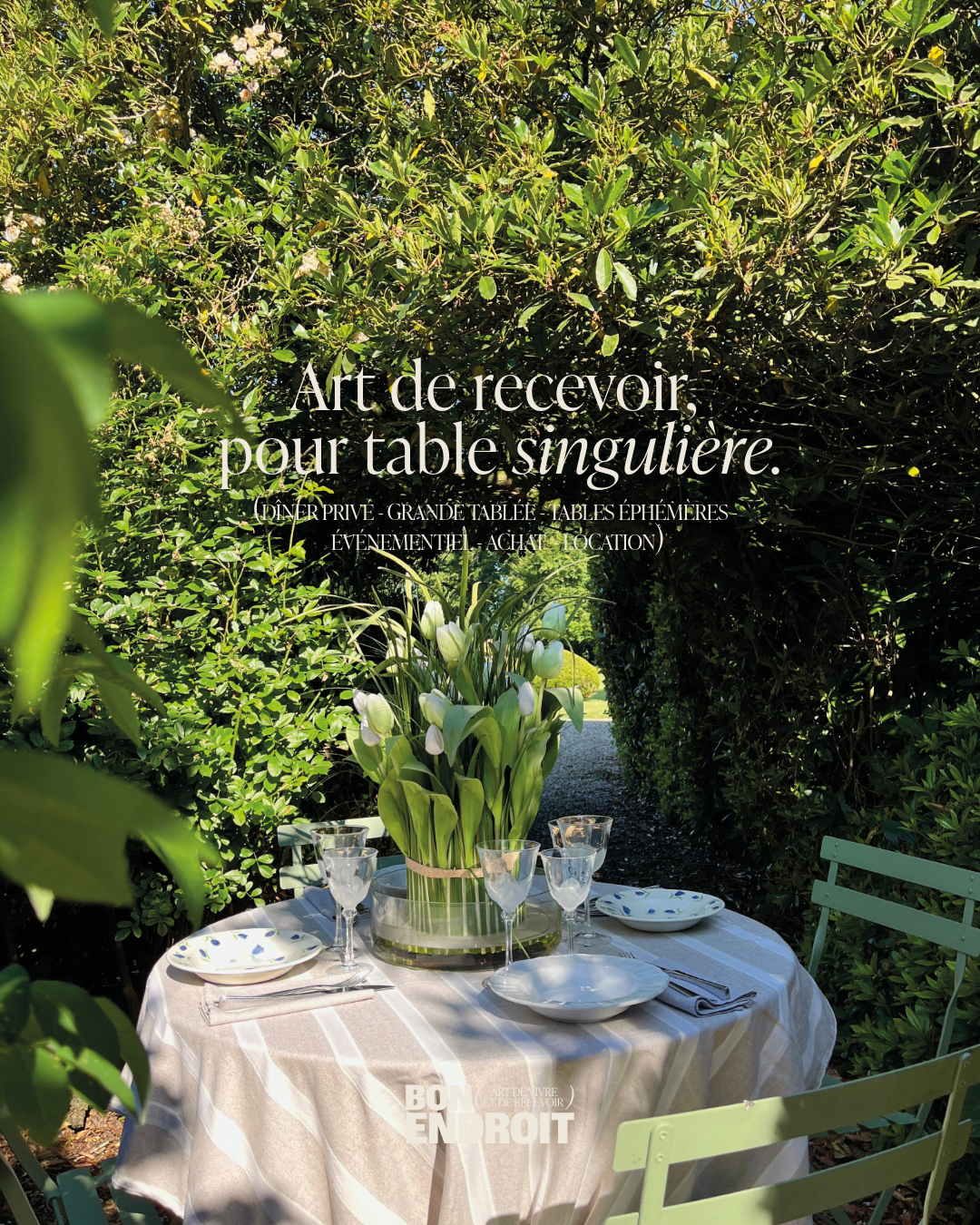 Table de jardin élégamment dressée avec de la vaisselle en mixte and math, a retrouver dans l'art de la table, des verres à vin, un vase avec des tulipes blanches, dans une atmosphère de jardin verdoyant pour un dîner privé ou un événement spécial.