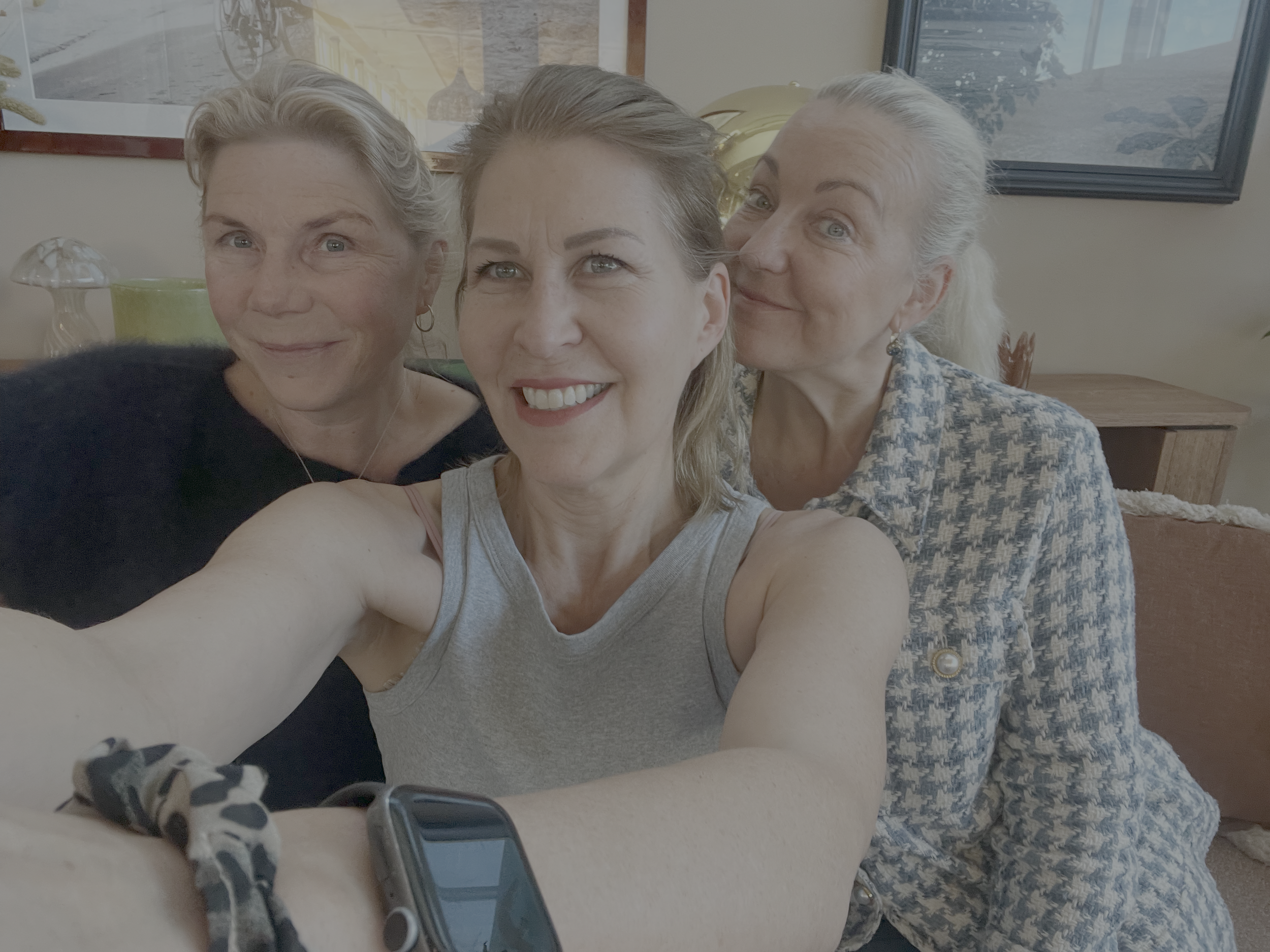 Three women smiling and taking a selfie together in a home setting.