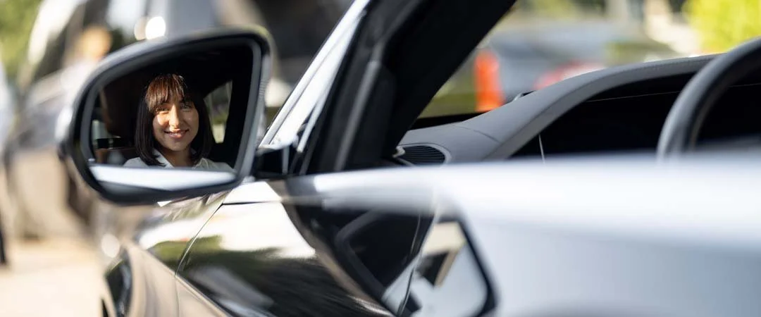 Foto eines Autospiegels, in dem man eine Frau lächeln sieht